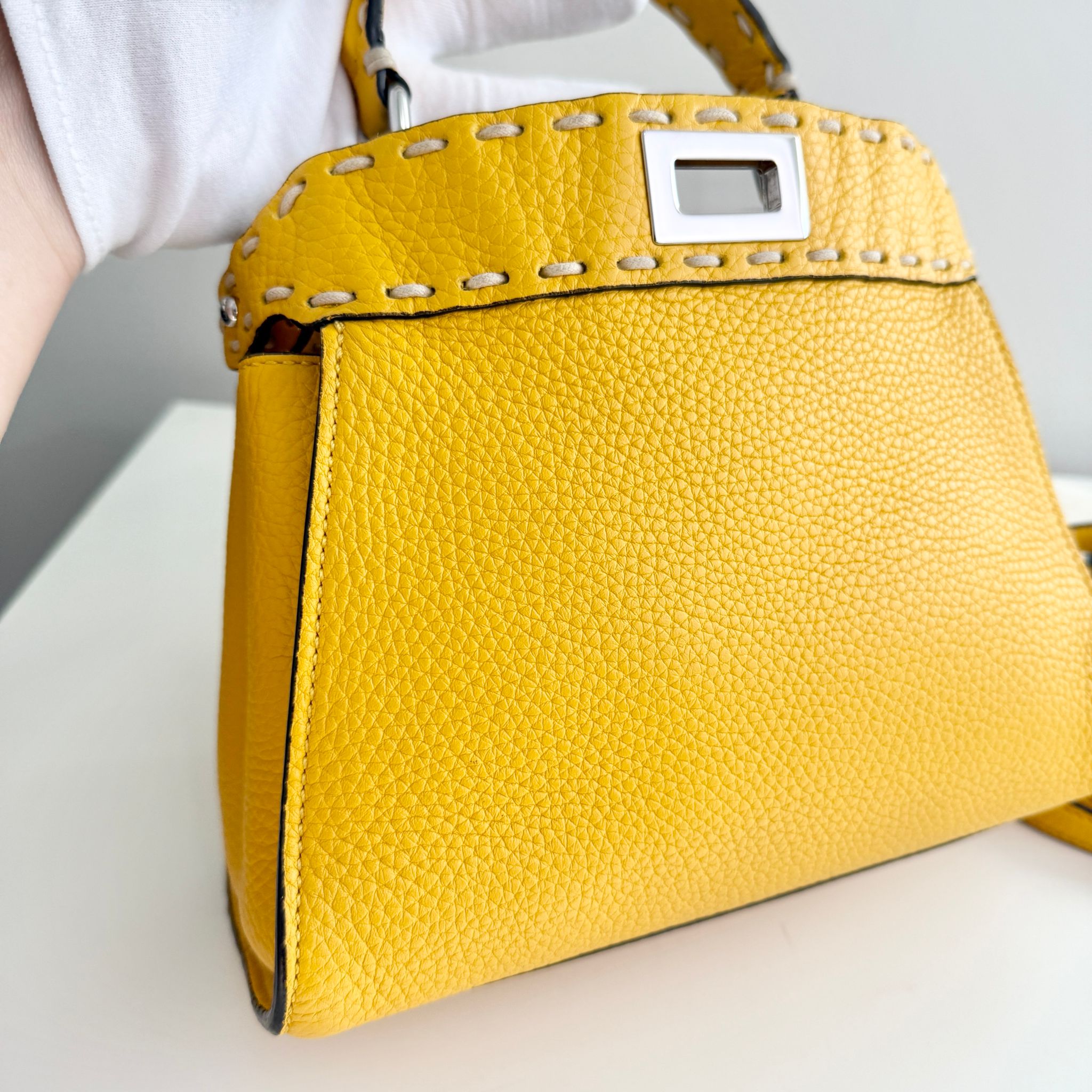 Yellow handbag with a textured surface and visible brand logo on a light background