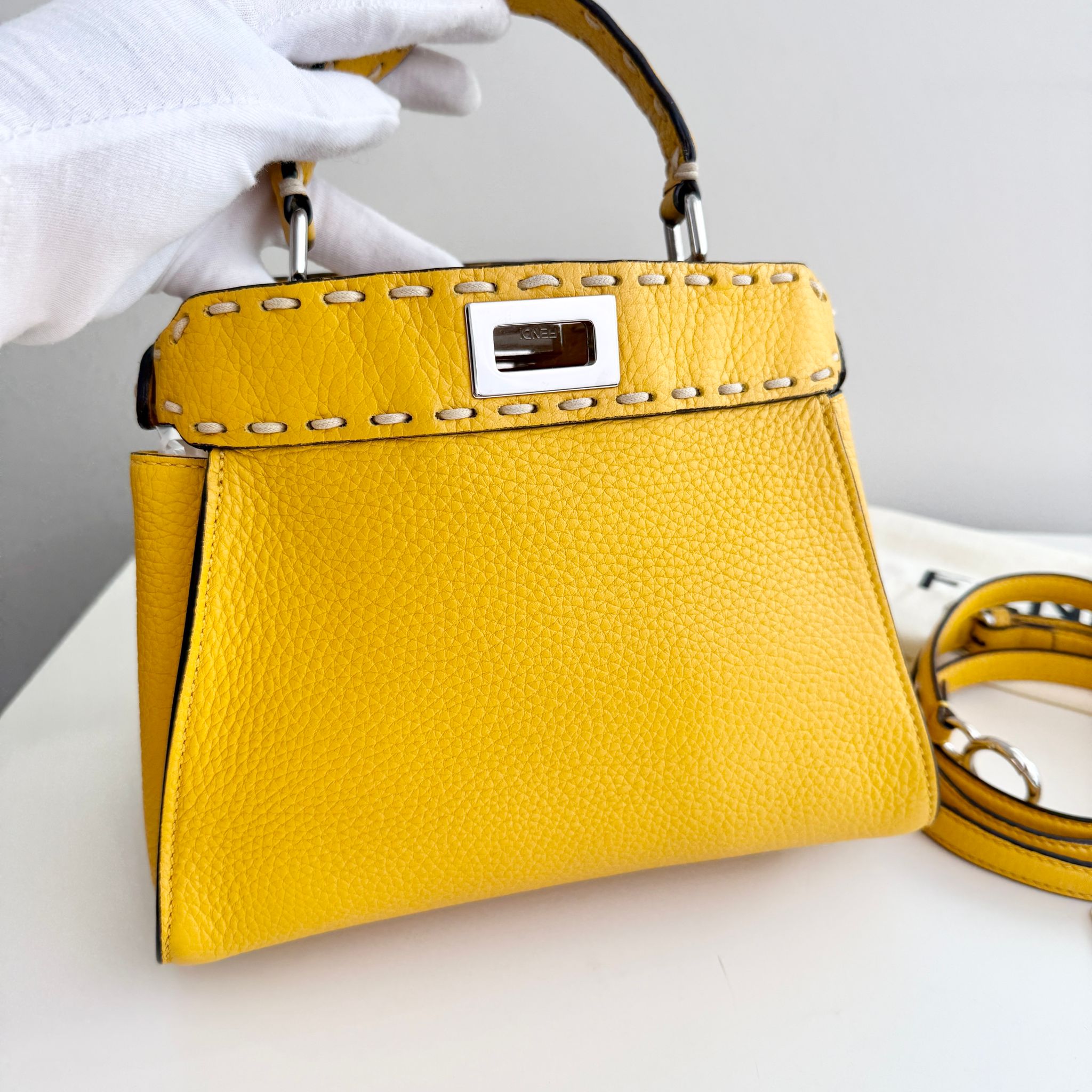 Yellow handbag with a silver clasp held by a gloved hand on a white background