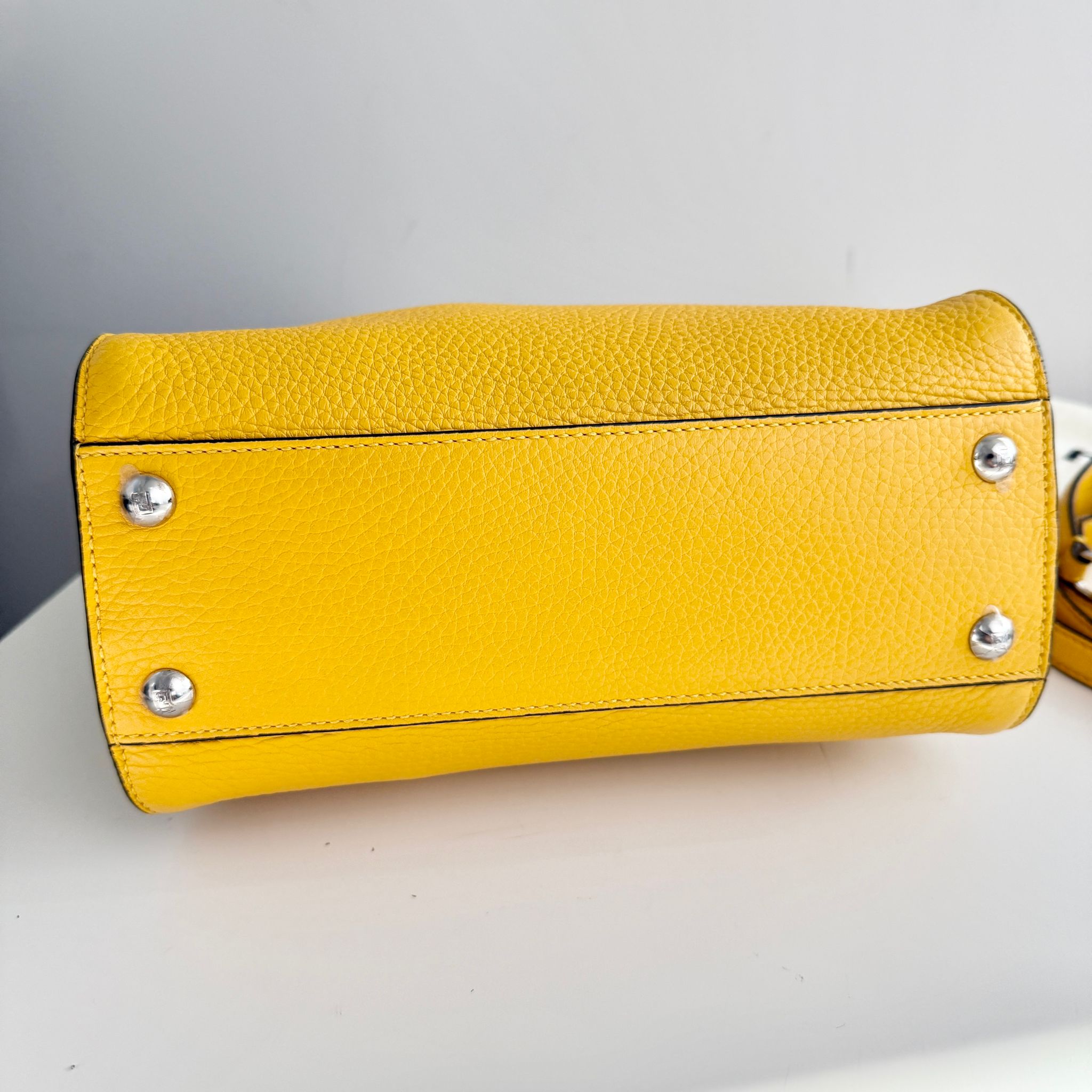 Yellow leather handbag with silver studs on a light gray background