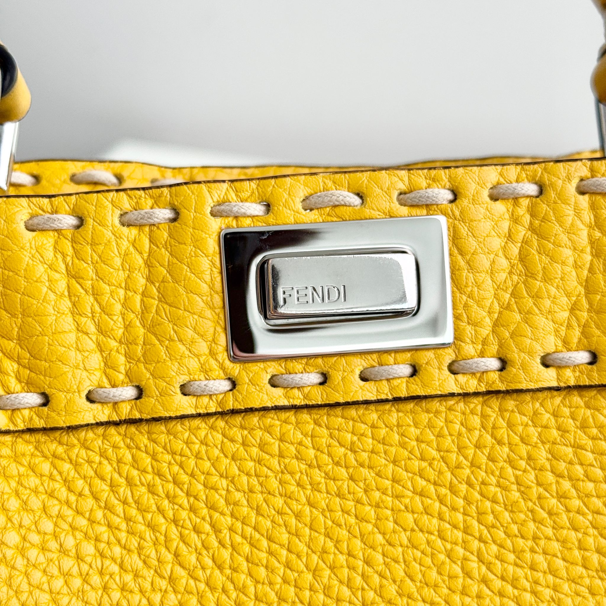 Close-up of a yellow leather handbag with a silver Fendi plaque.