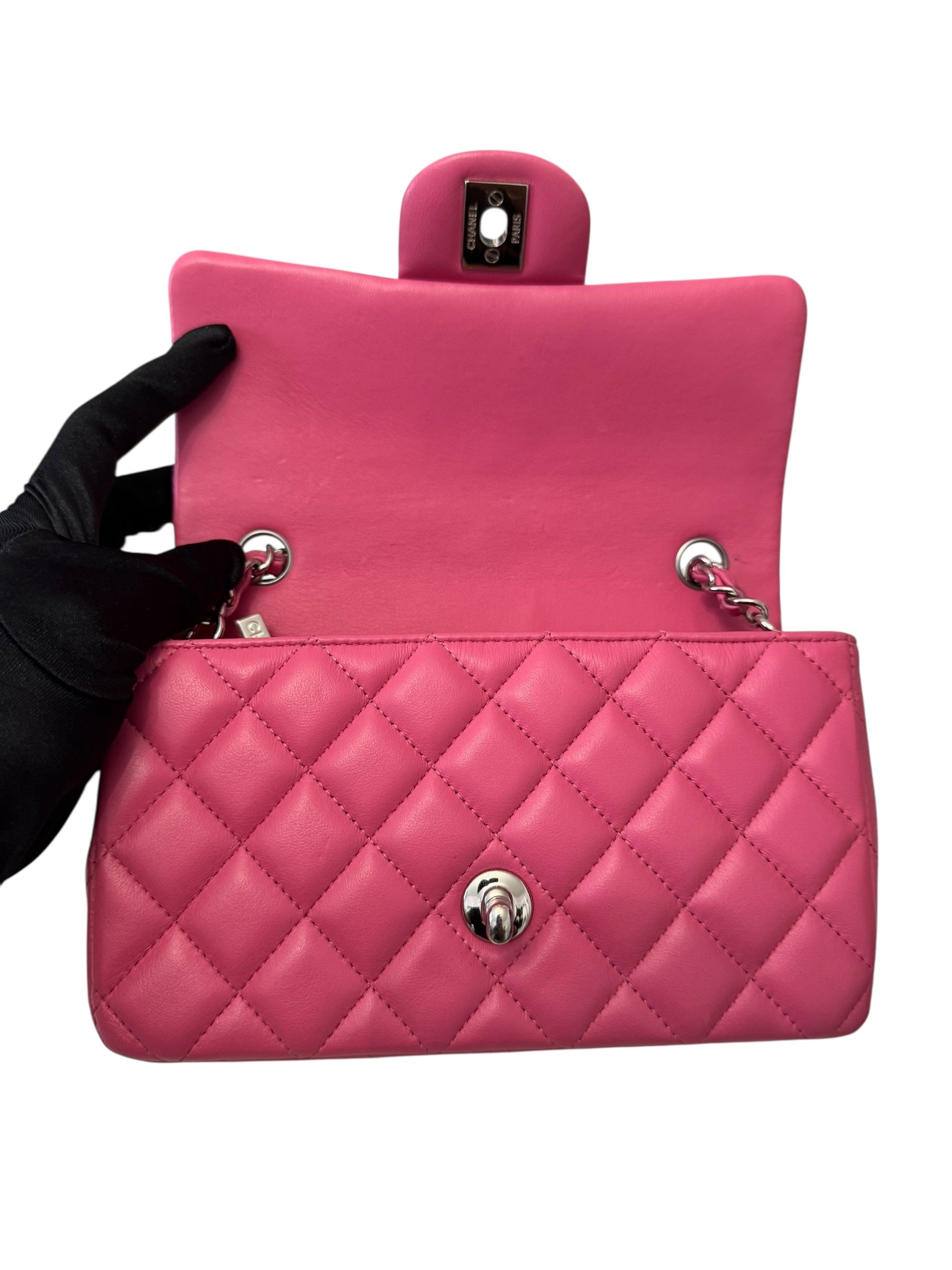 Pink quilted handbag with a black glove holding it on a white background
