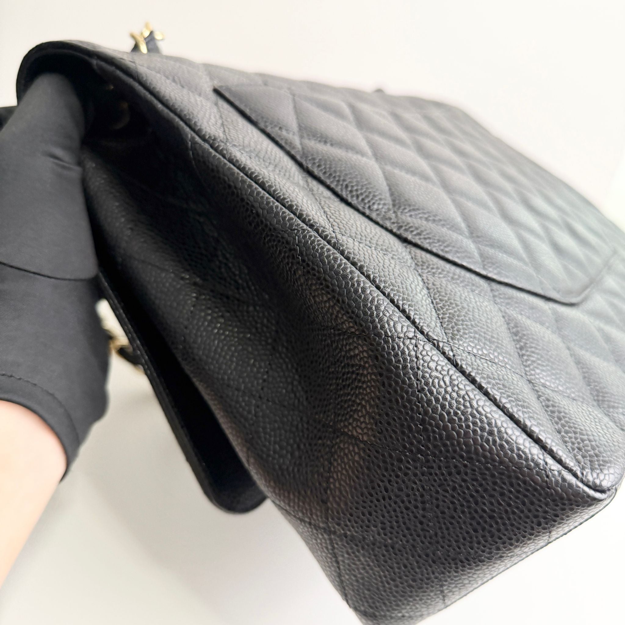 Black quilted handbag held by a gloved hand on a white background