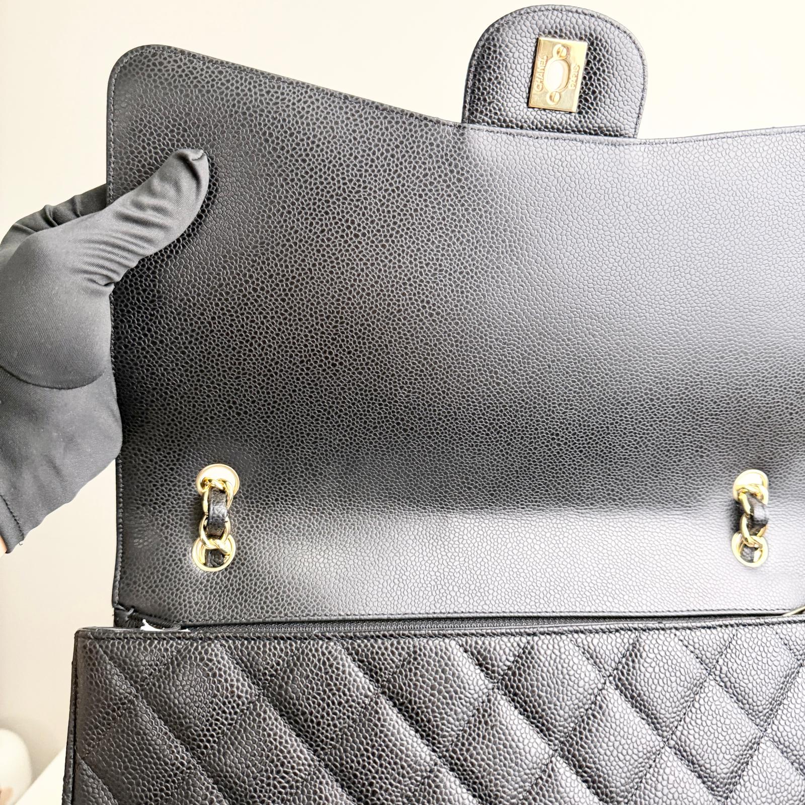 Black handbag with gold hardware held by a person wearing gray gloves.