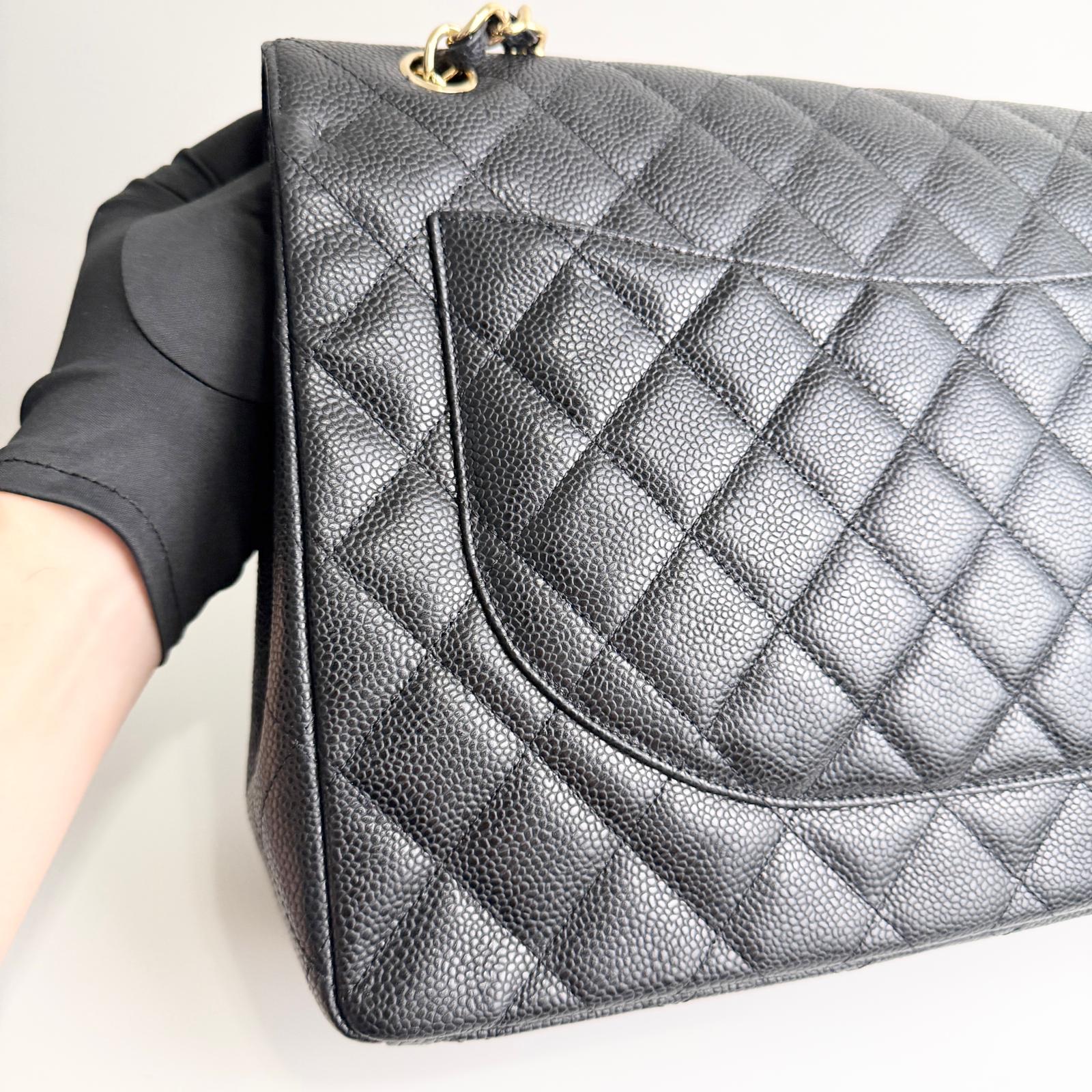 Black quilted handbag held by a person on a light gray background