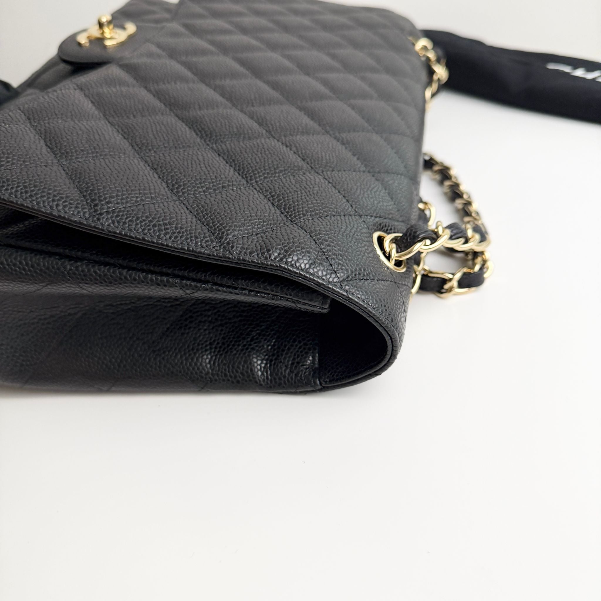 Black quilted handbag with gold chain on a light gray background