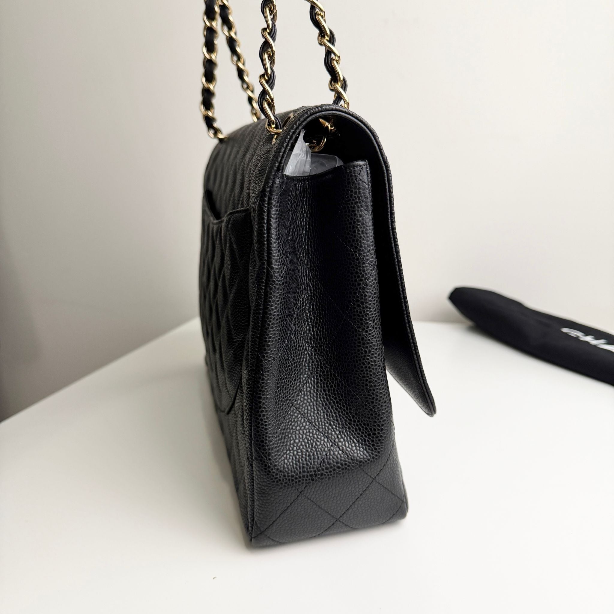 Black quilted handbag with gold chain strap on a white surface