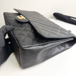 将图片加载到图库查看器，Black quilted handbag with gold clasp held by a gloved hand on a white background
