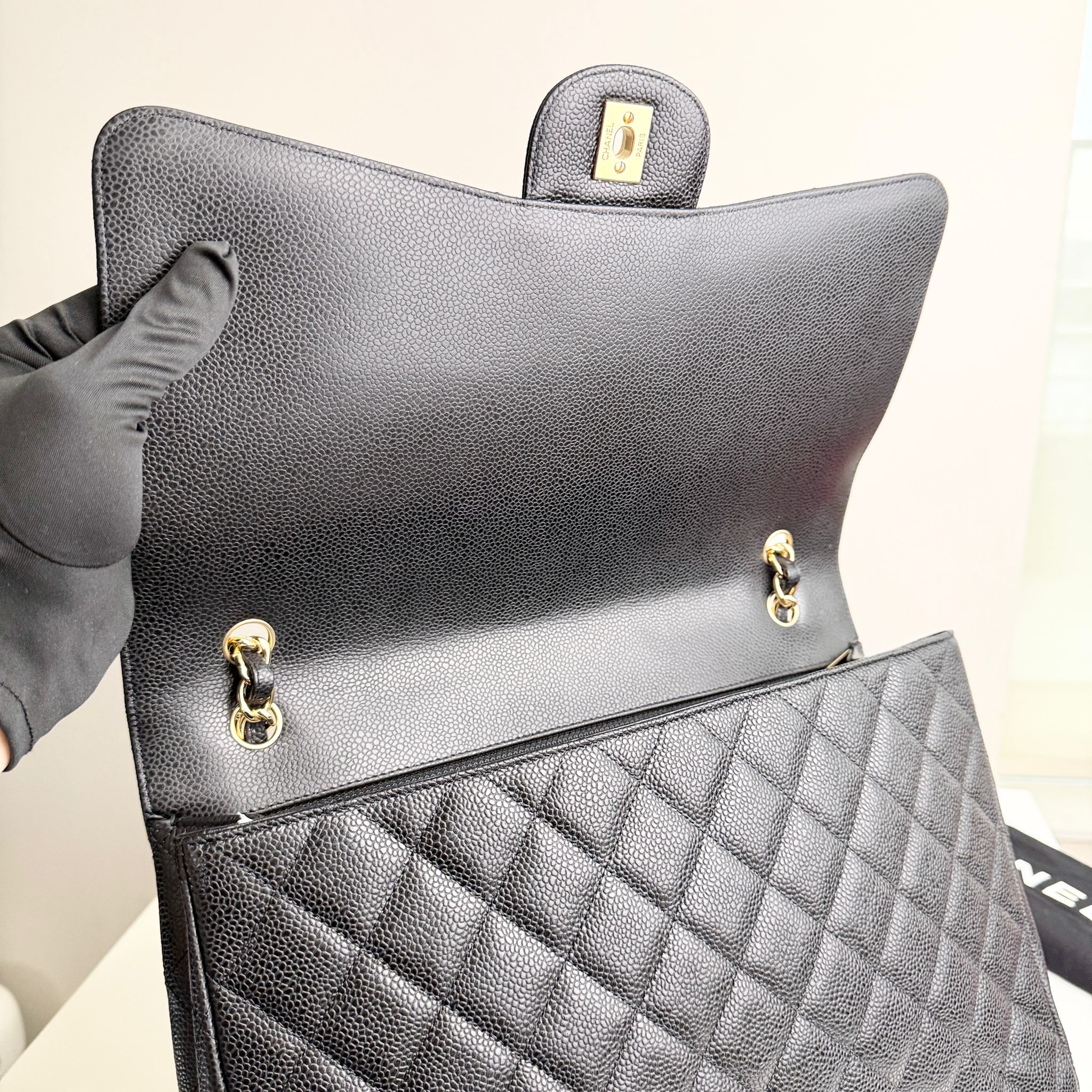 Gray quilted handbag with gold hardware held by a gloved hand against a neutral background