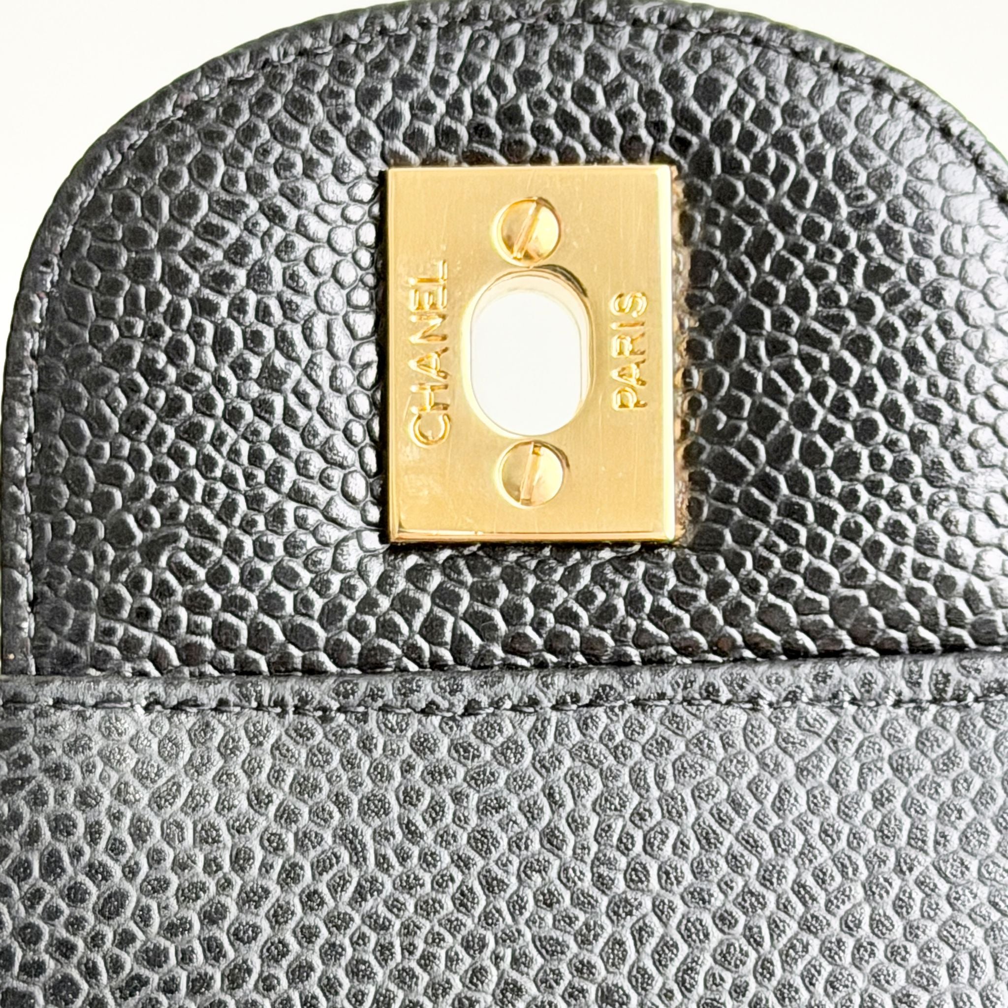Close-up of a black textured handbag with a gold Chanel logo.
