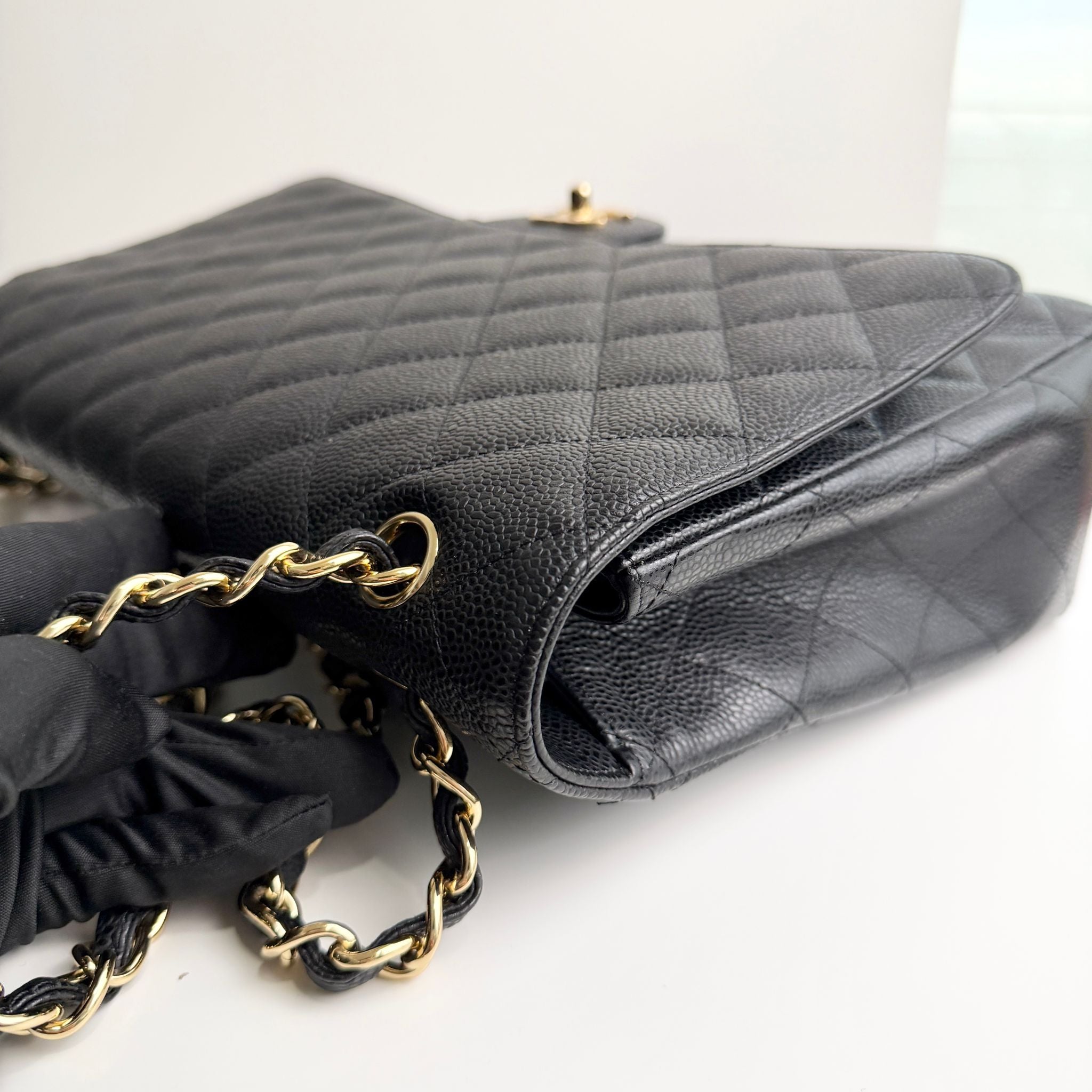 Black quilted handbag with gold chain on a white background