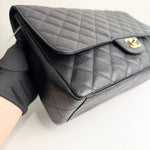 将图片加载到图库查看器，Black quilted handbag with gold clasp held by a gloved hand on a light background
