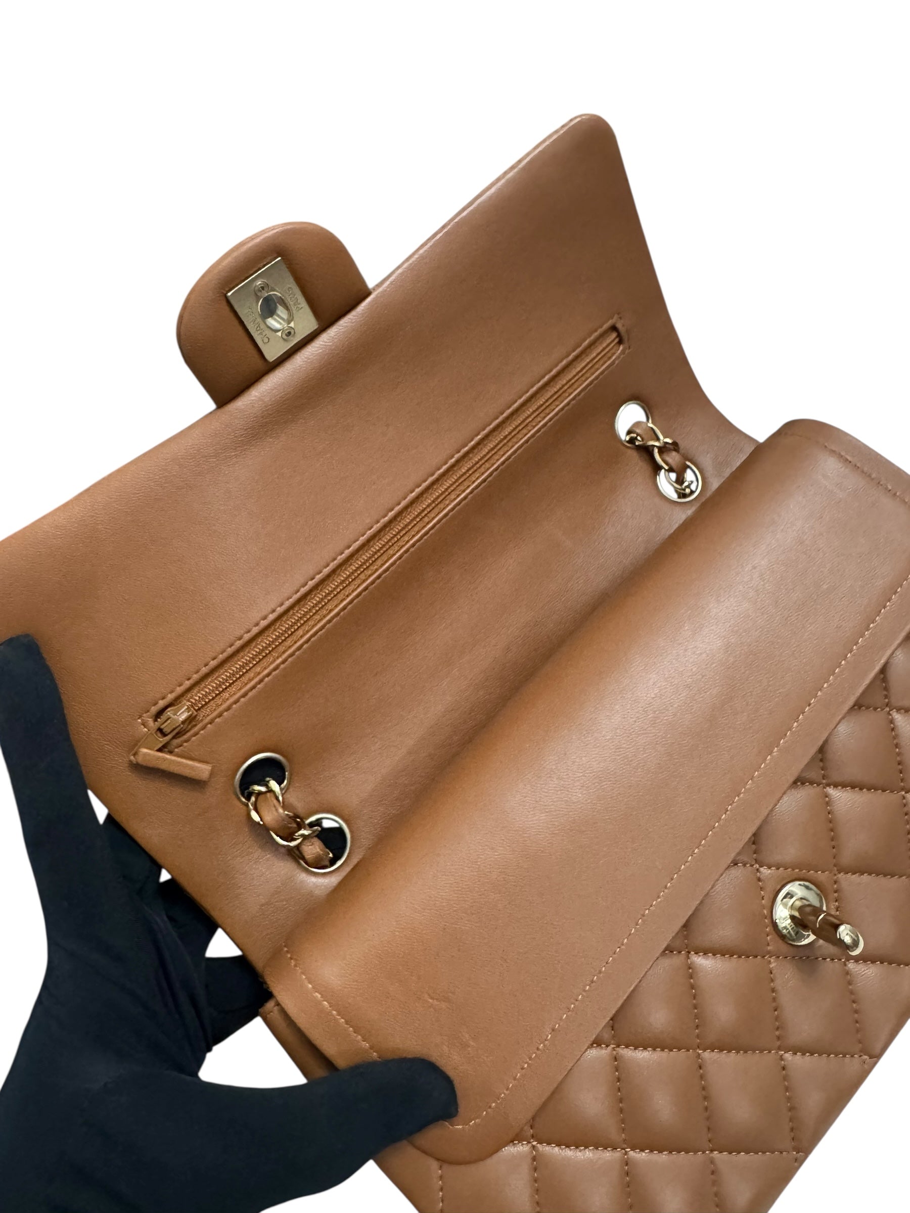 Brown leather handbag with gold hardware held by a gloved hand on a white background