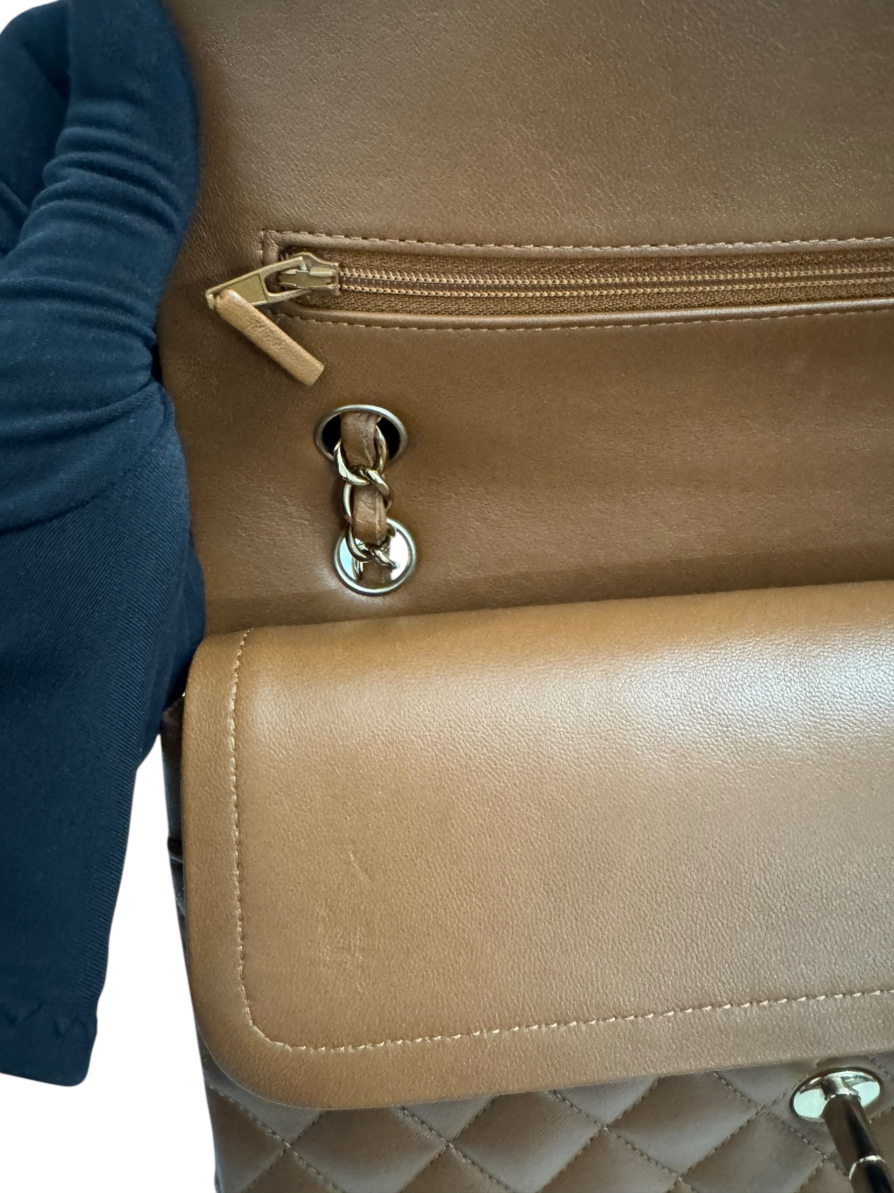 Close-up of a beige handbag with a gold zipper and chain detail.