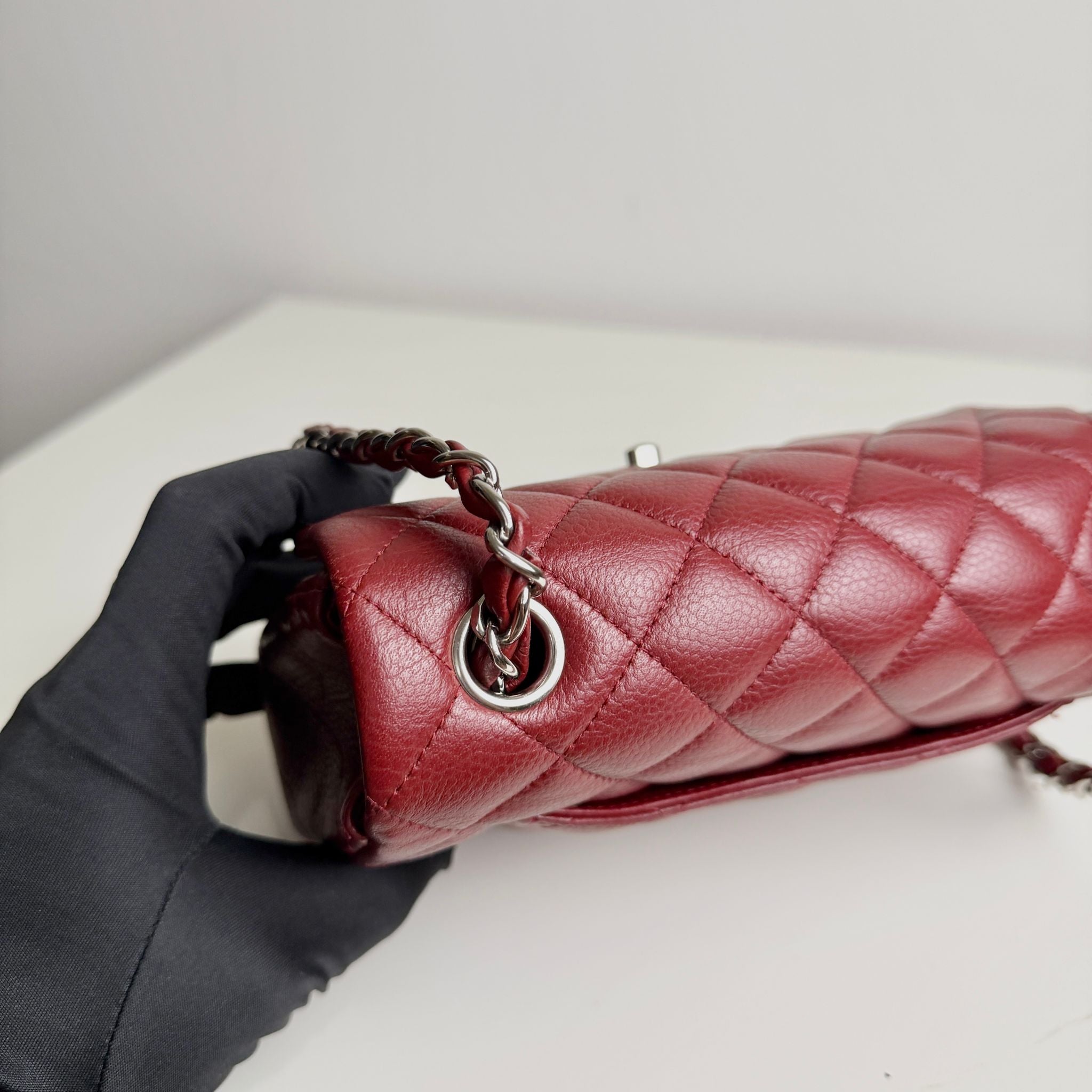 Red quilted handbag with gold chain handle held by a gloved hand on a light background