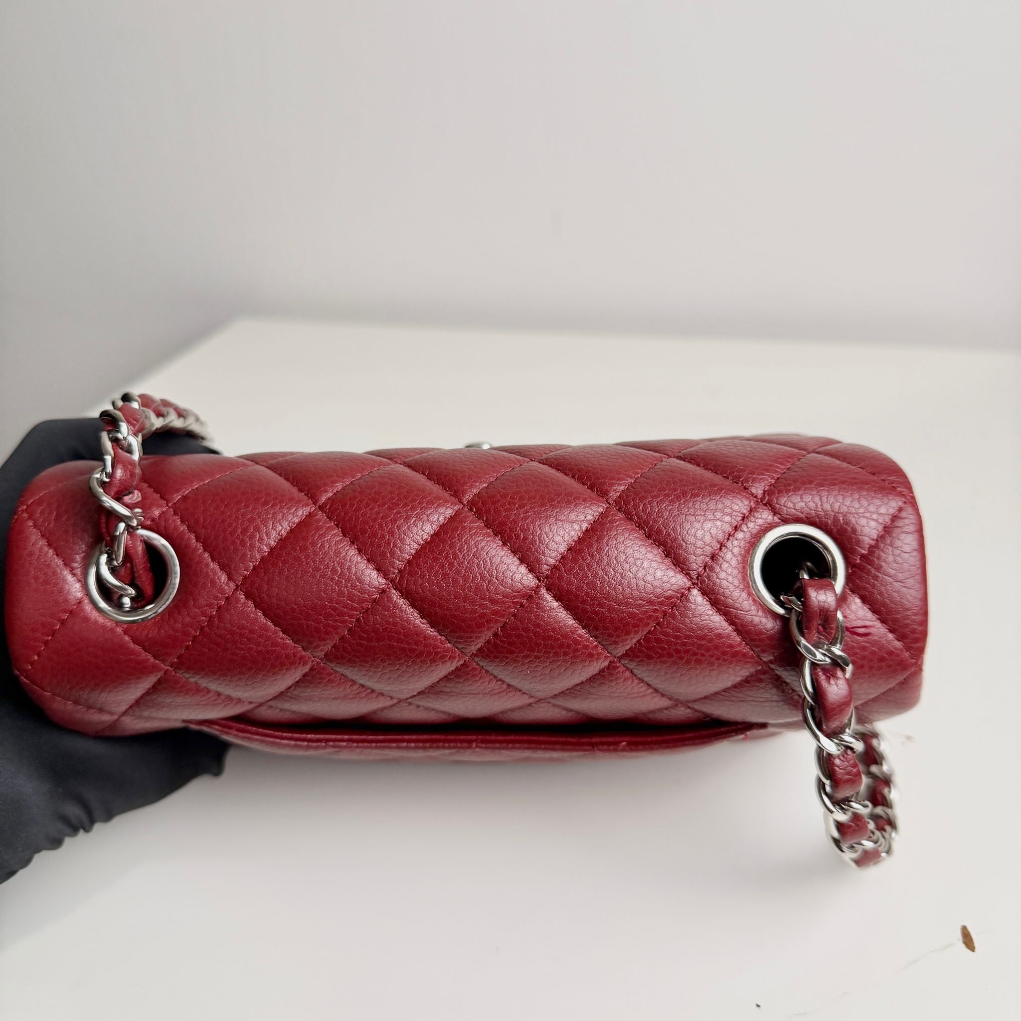 Red quilted handbag with chain detail held by a gloved hand on a light background
