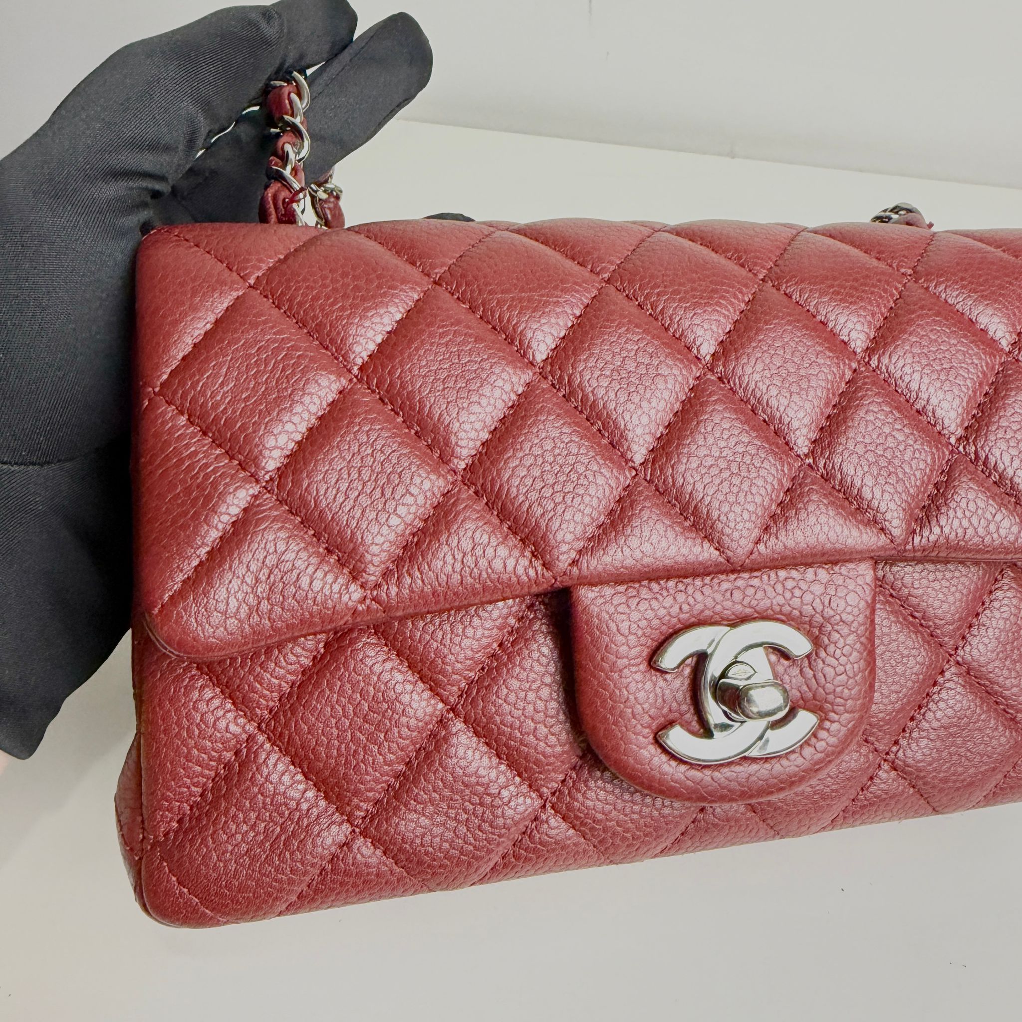 Red quilted handbag with Chanel logo held by a gloved hand on a light background