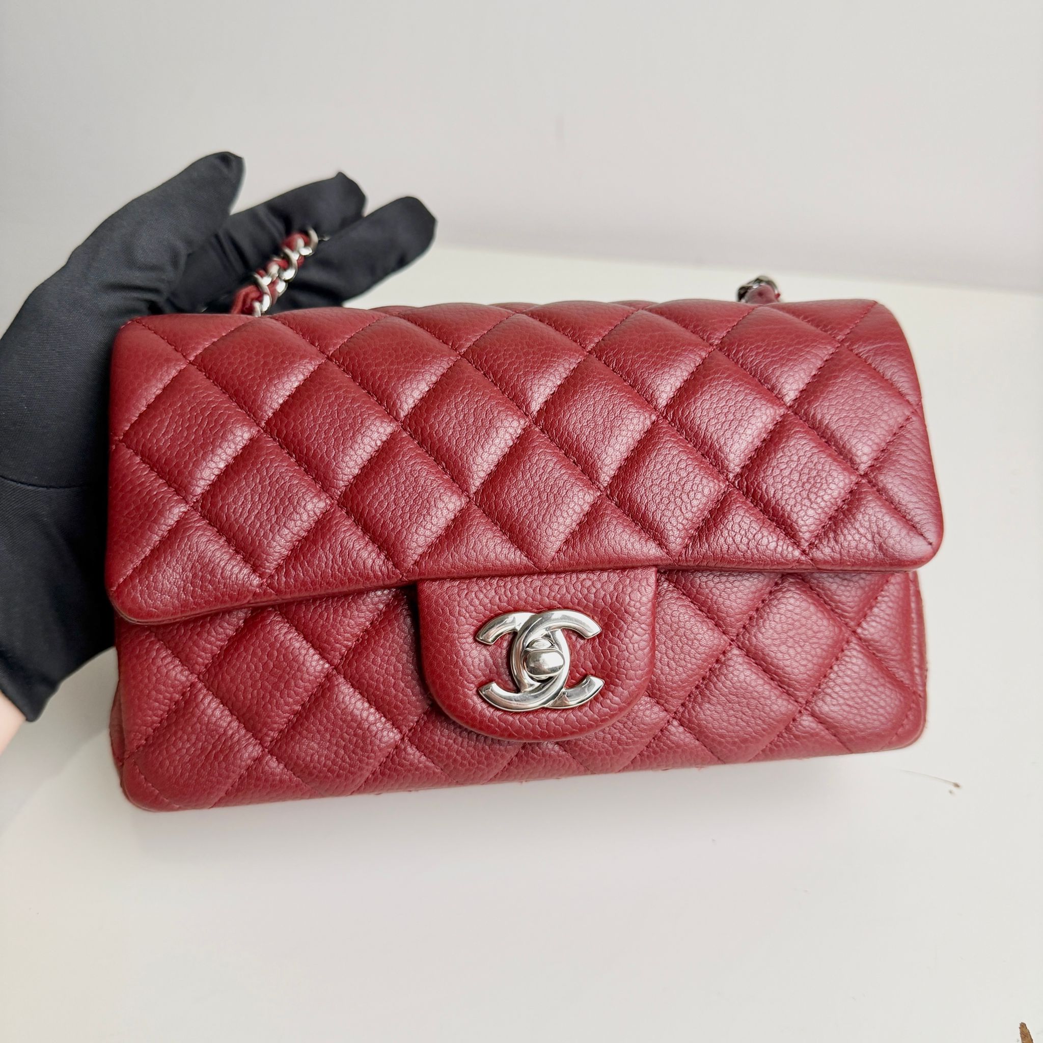 Red quilted handbag with Chanel logo held by a gloved hand on a white background