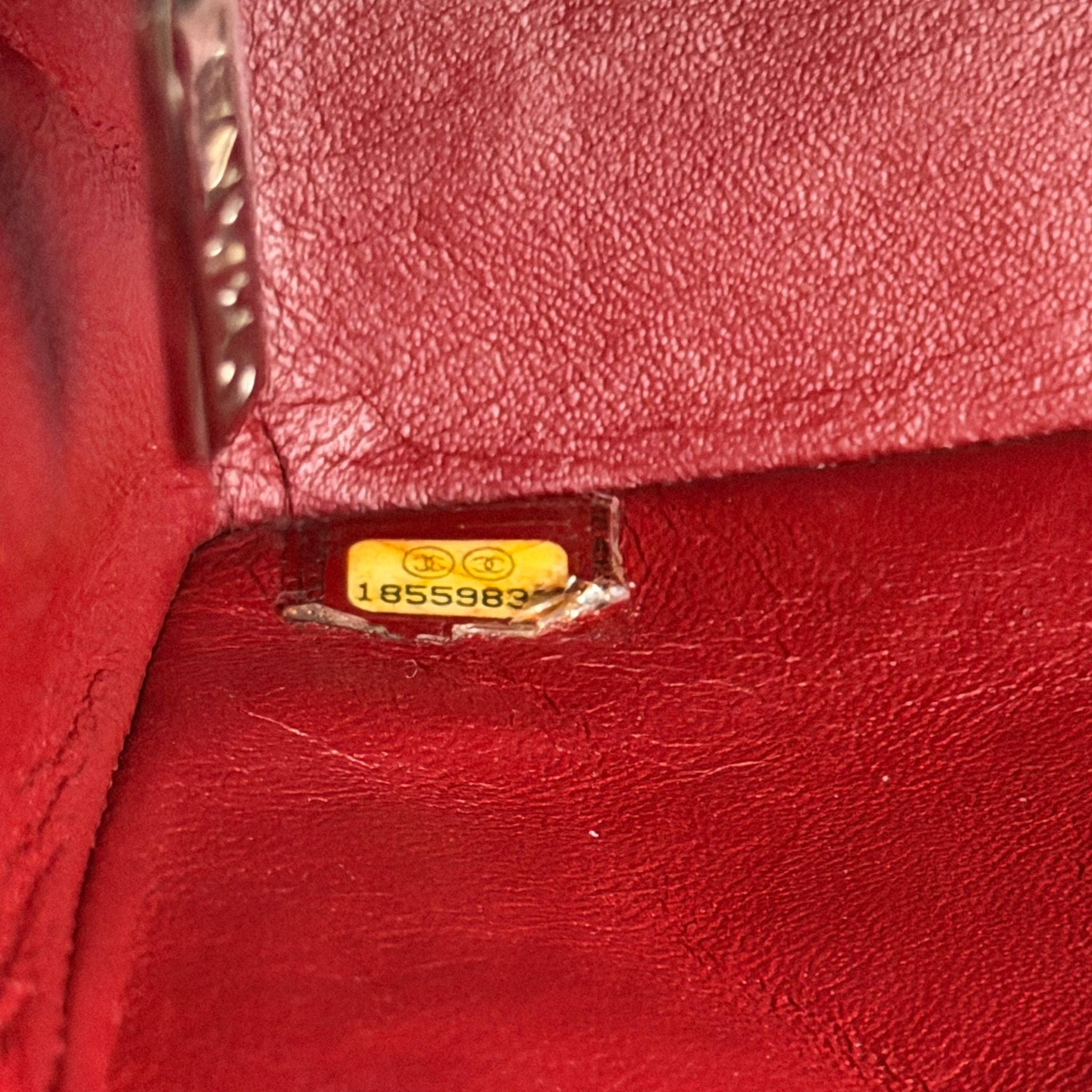 Close-up of a red leather product with a gold tag and number on a textured surface.