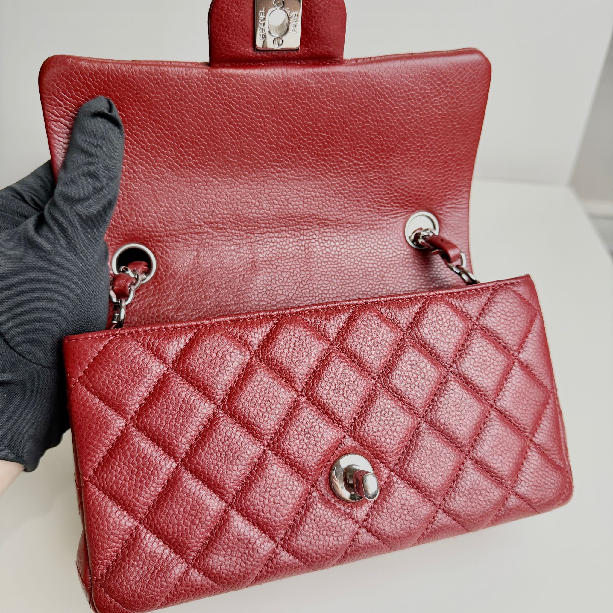 Red quilted handbag held by a gloved hand on a light background