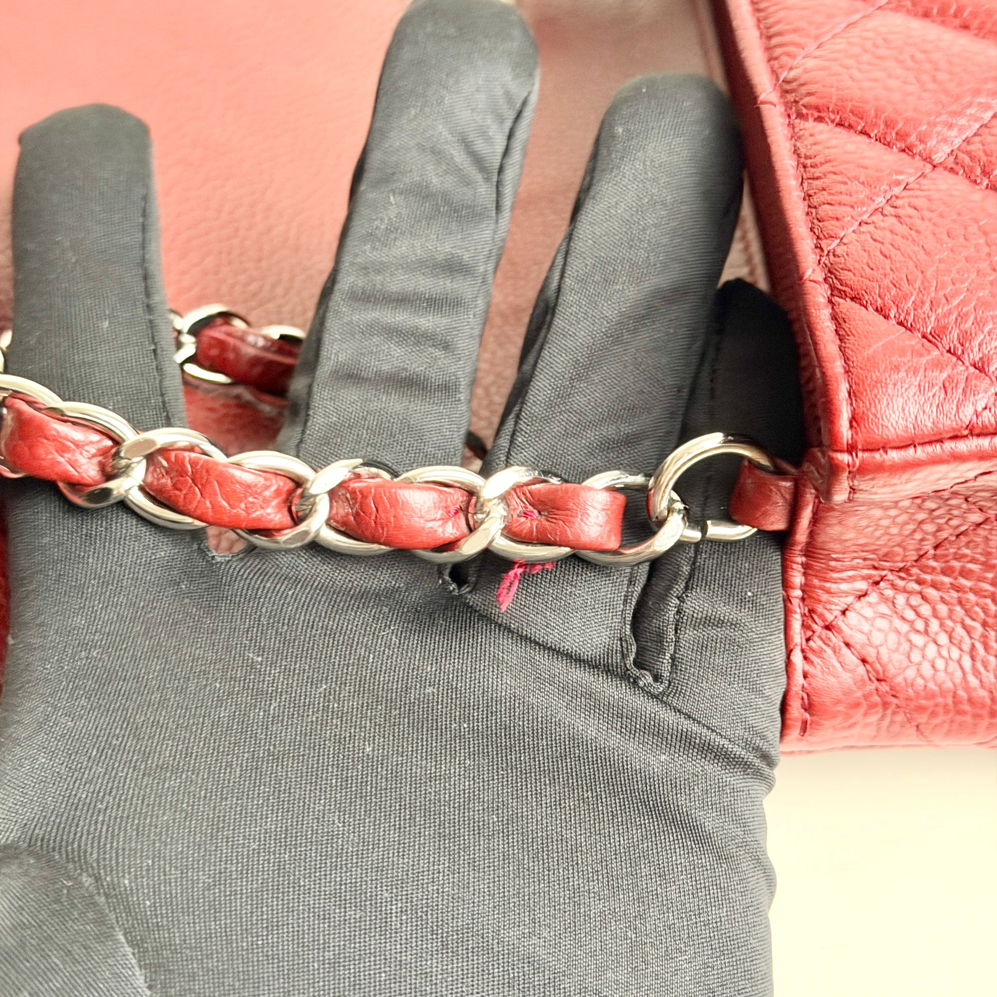 Red leather bracelet with silver chain on a gray glove against a red textured background