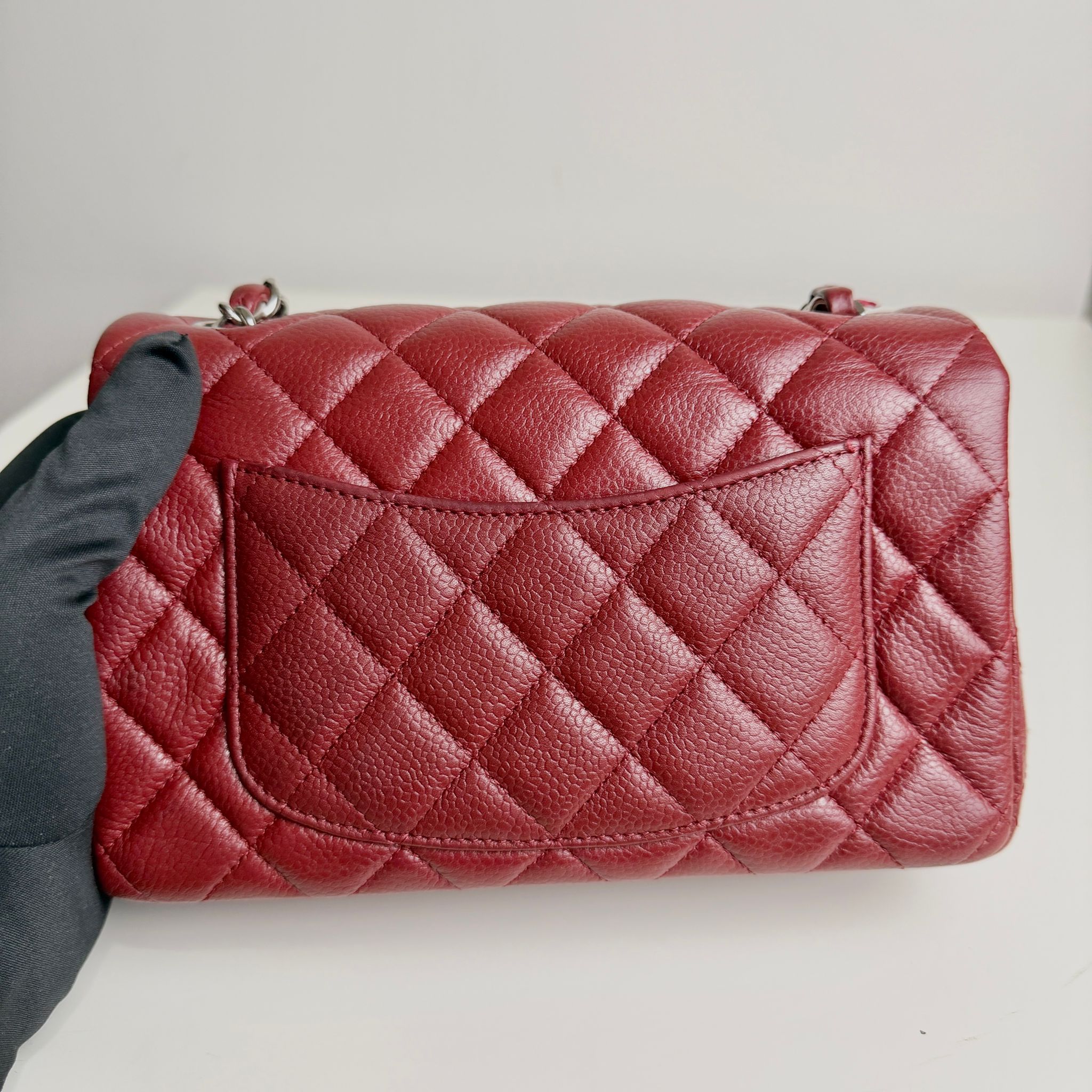 Red quilted handbag on a white surface with a gray background