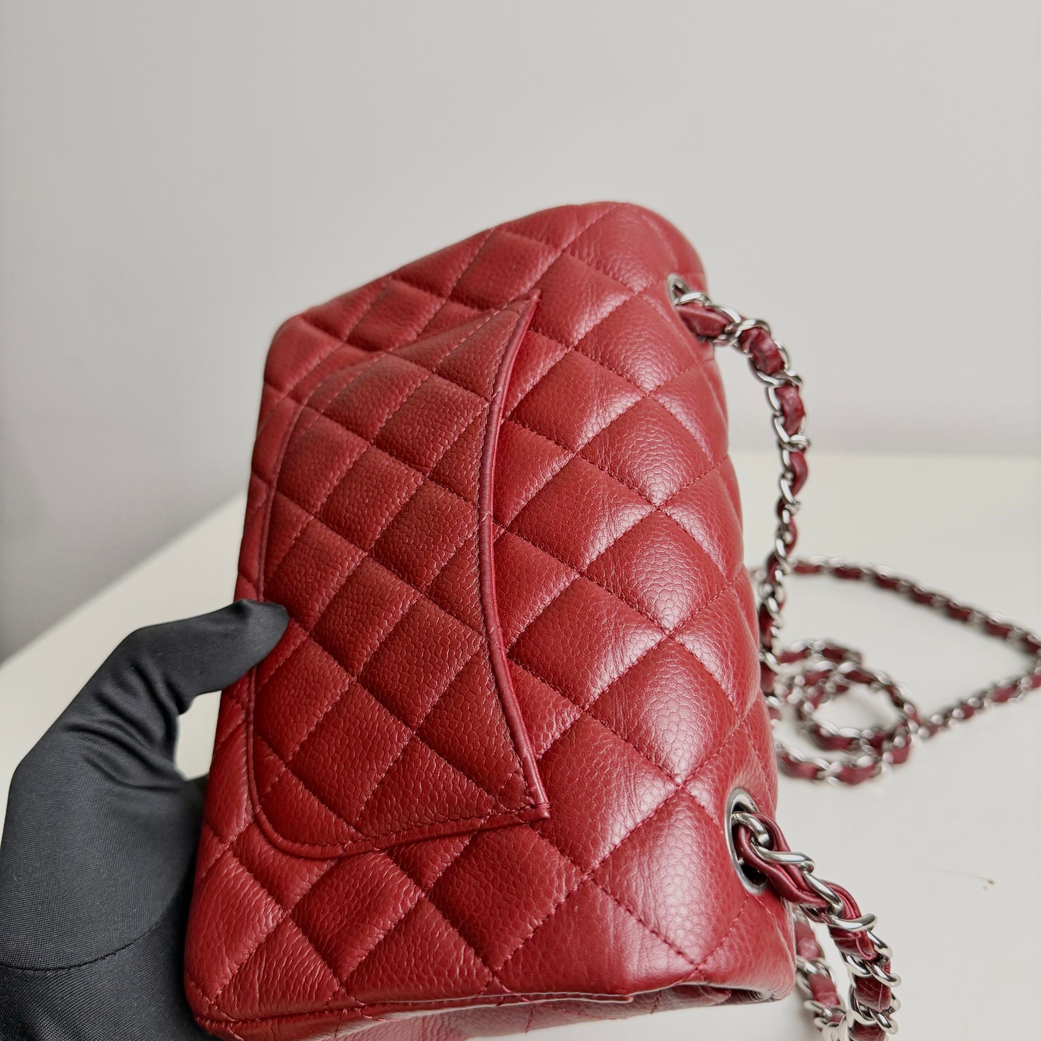 Red quilted handbag with a chain strap held by a gloved hand against a neutral background