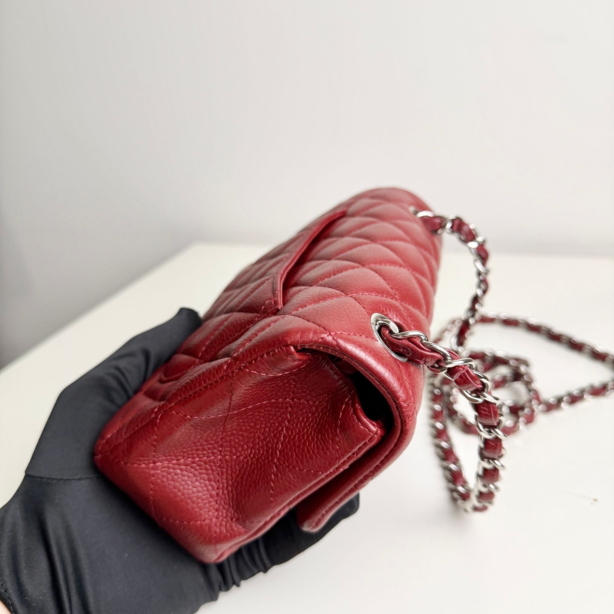 Red quilted handbag with a chain strap held by a gloved hand on a light background