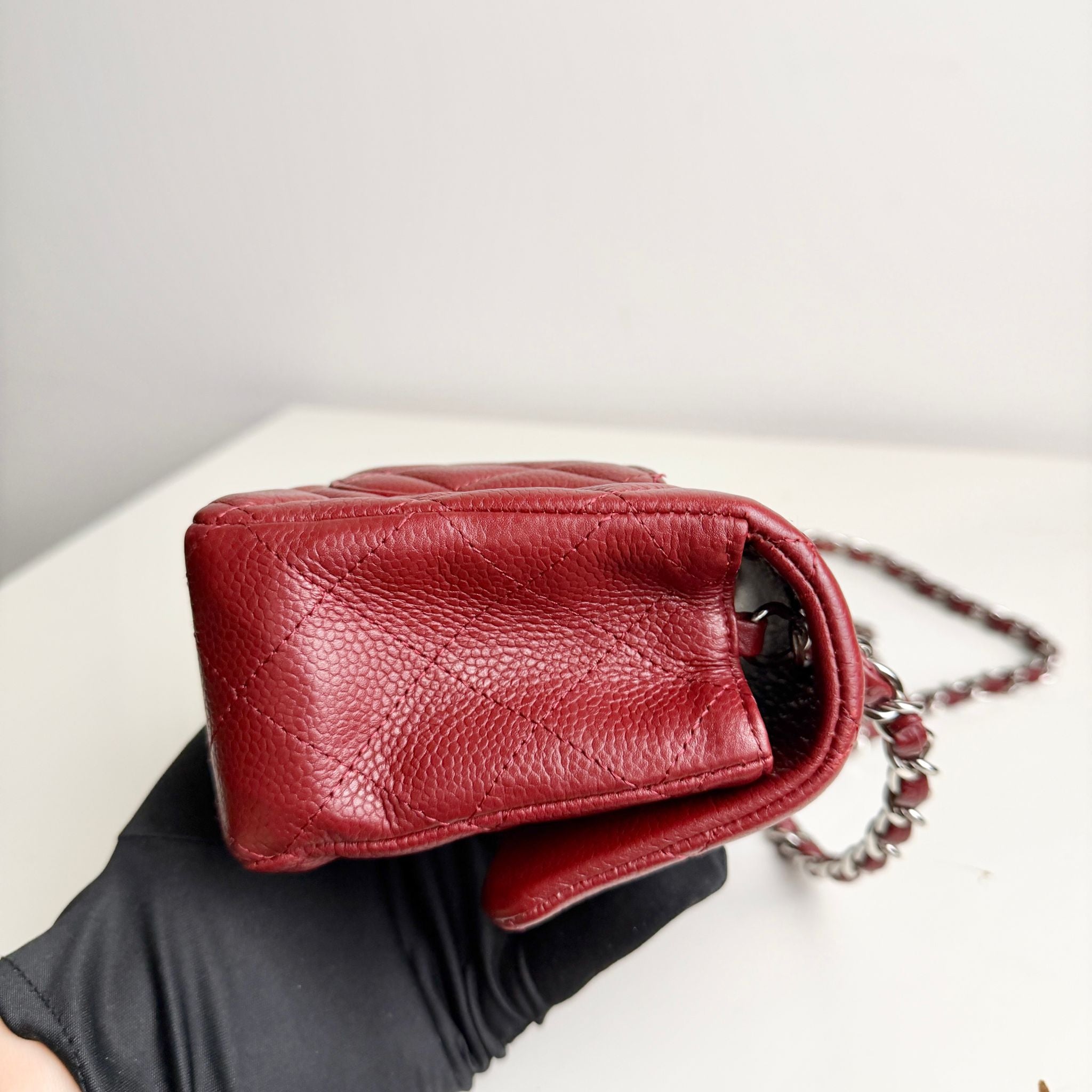 Red leather handbag with a chain strap held by a gloved hand on a light background