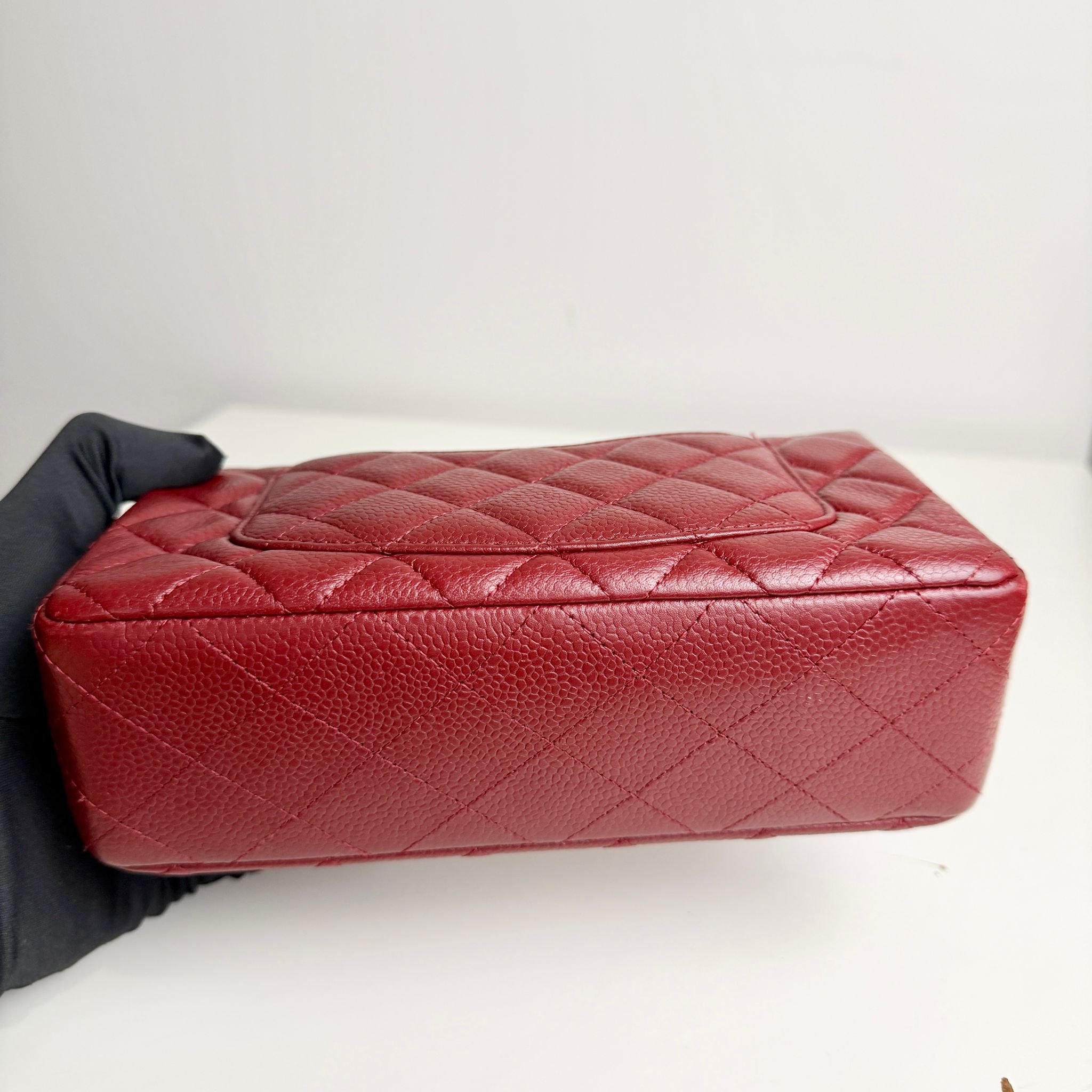 Red quilted handbag held by a gloved hand on a white background