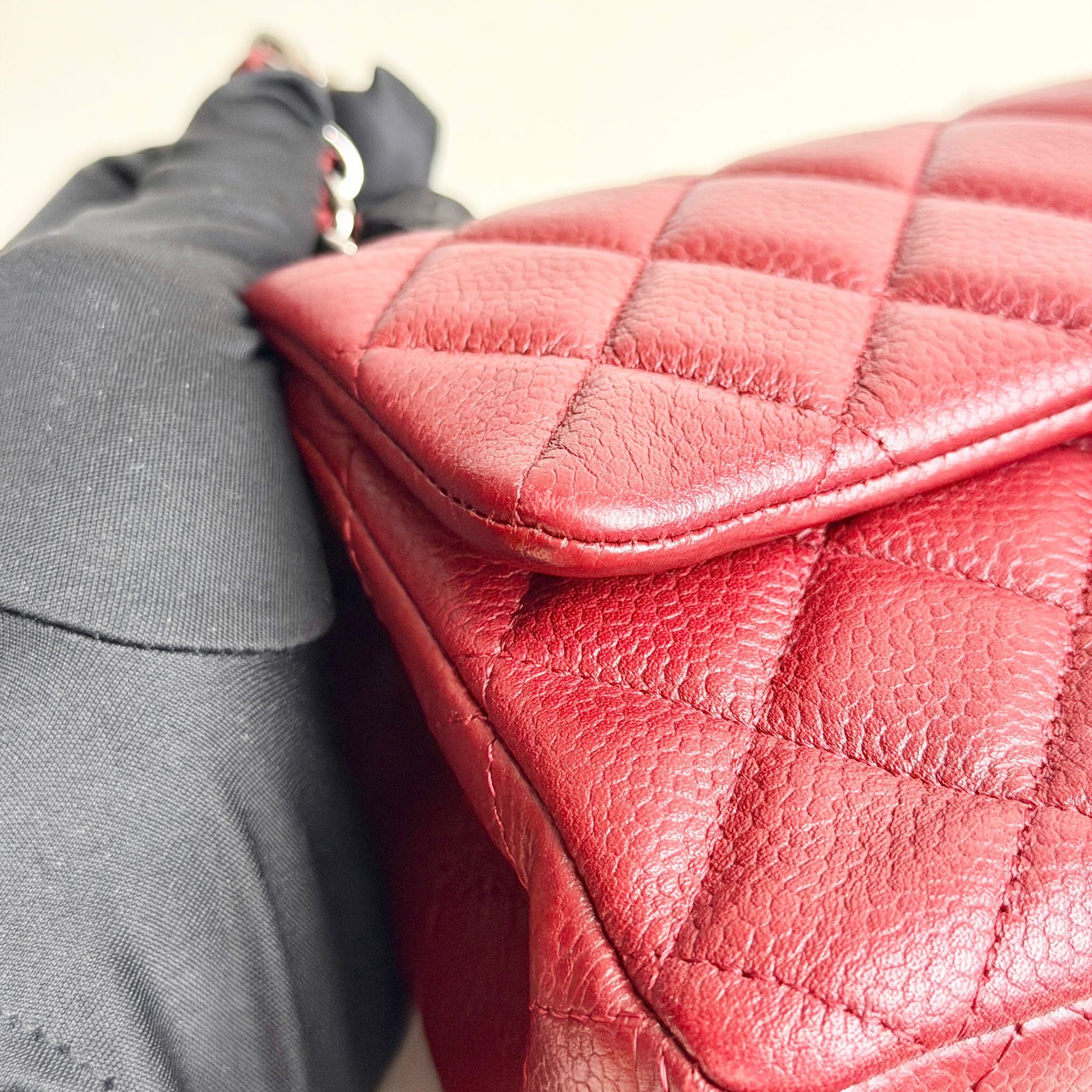 Close-up of a red quilted handbag with a gray coat next to it.