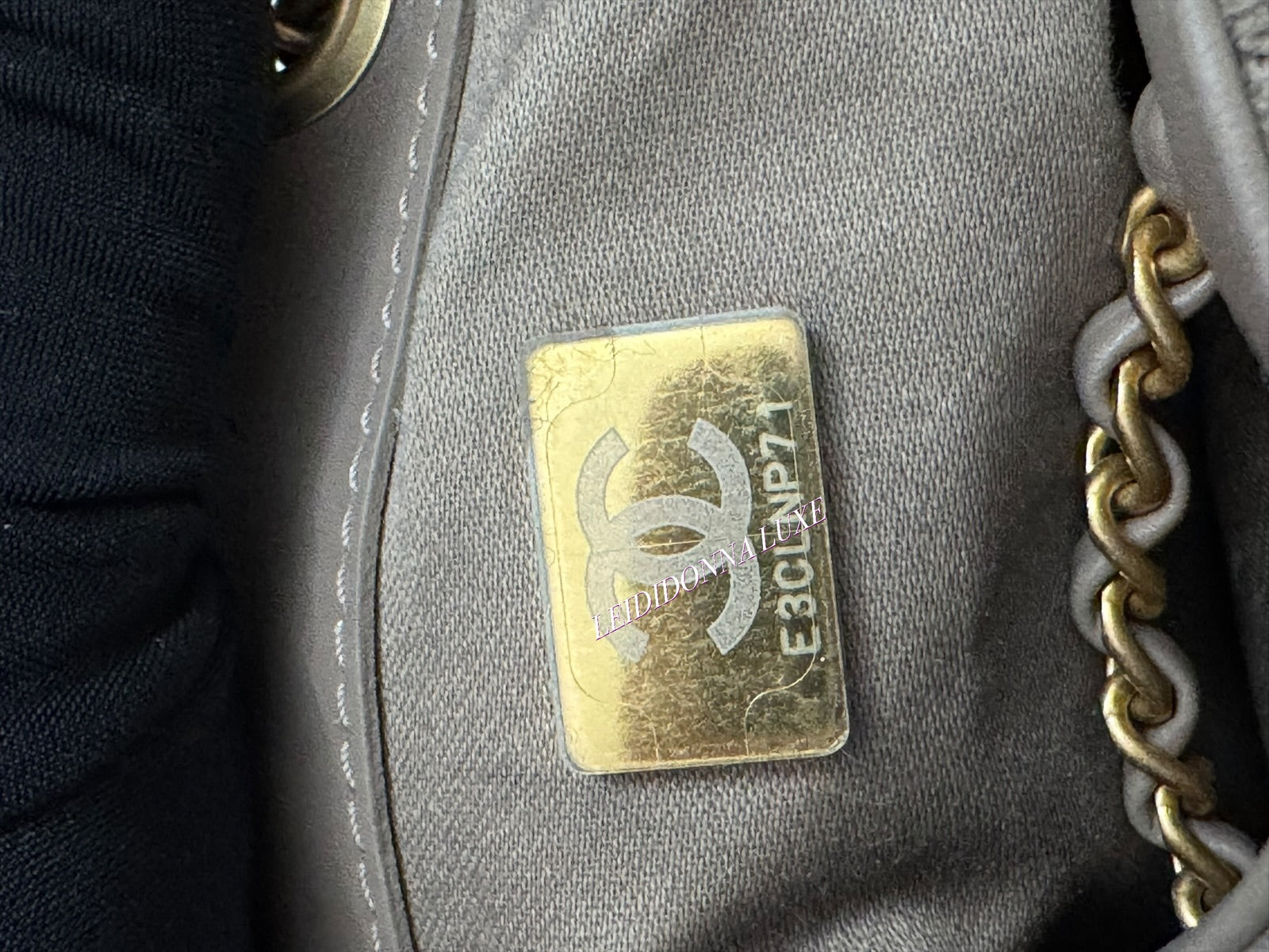 Close-up of a Chanel logo on a gray handbag with gold chain.