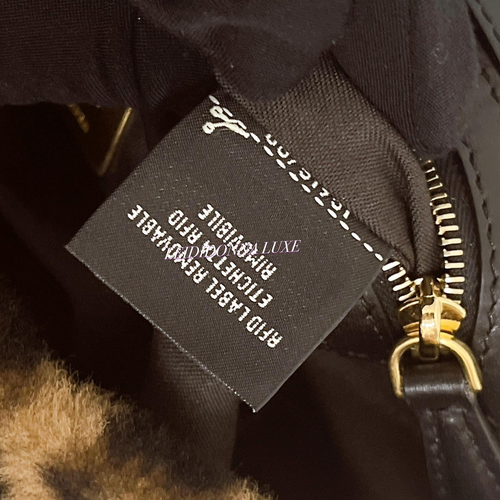 Close-up of a branded tag on a black leather product with gold zipper.