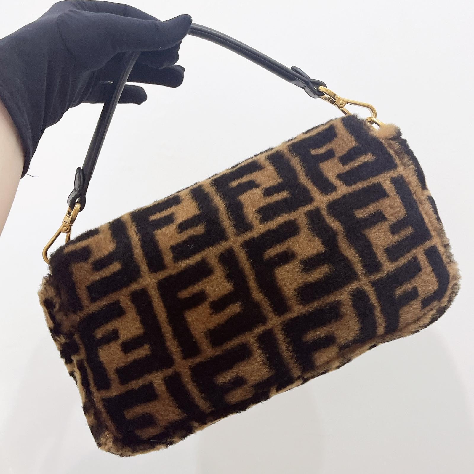 Brown handbag with black pattern held by a gloved hand on a white background