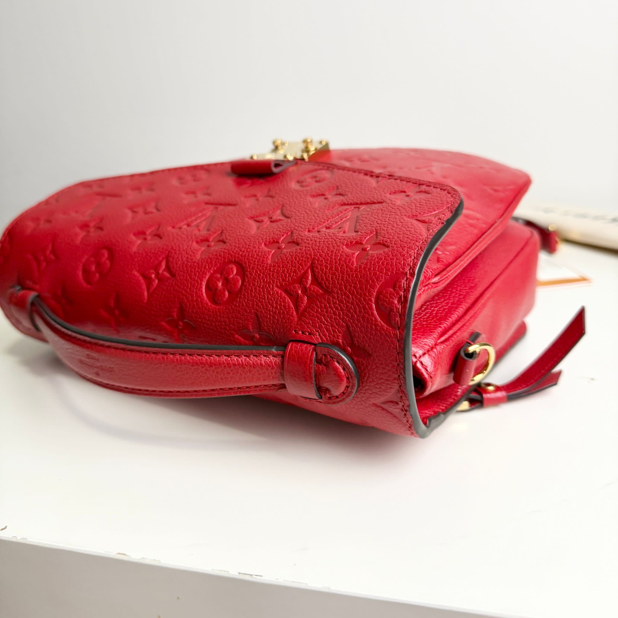 Red leather handbag with gold accents on a white surface