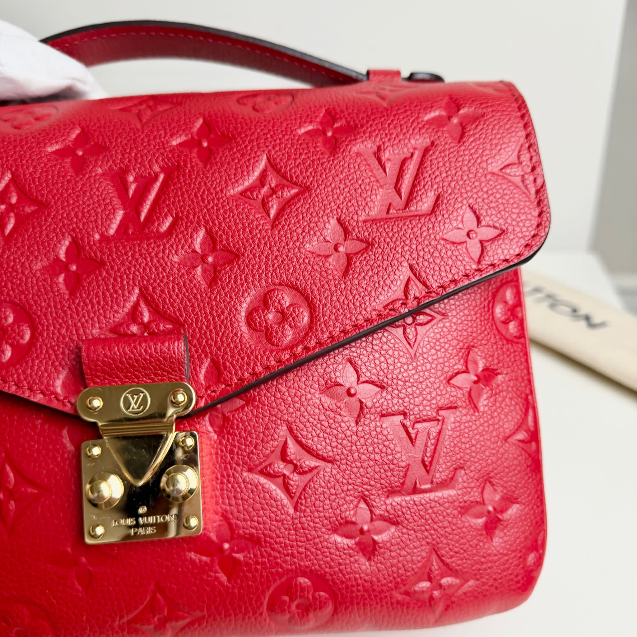 Red handbag with gold lock and Louis Vuitton monogram pattern on a white background