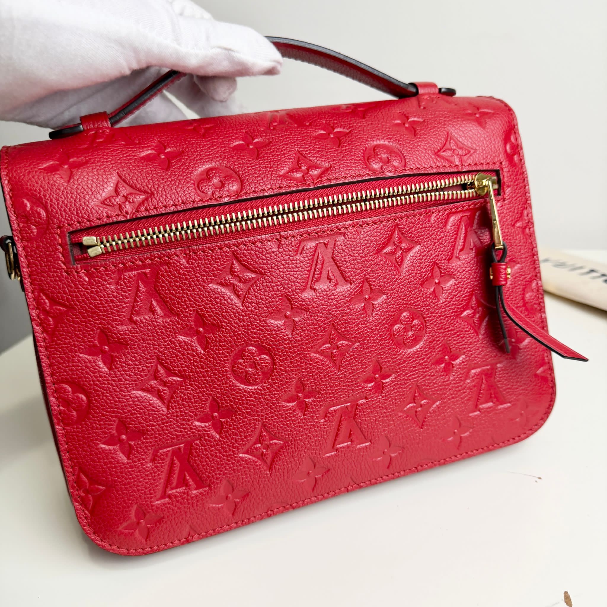 Red handbag with a brand logo held by a gloved hand on a white background