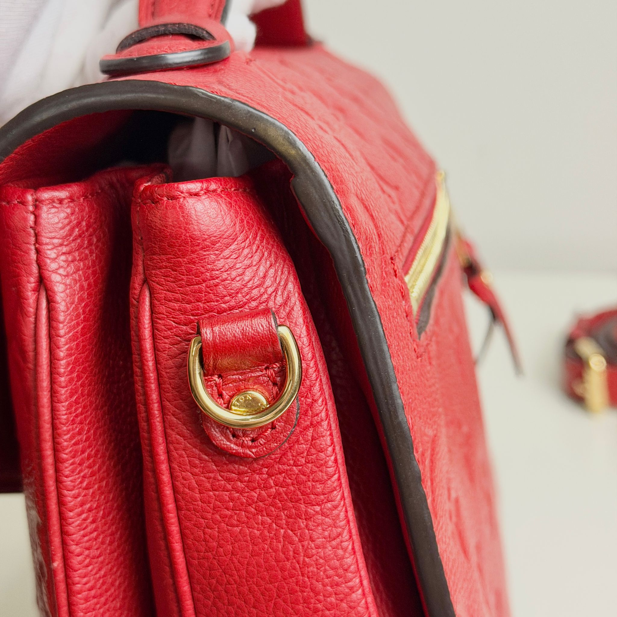 Close-up of a red leather handbag with a gold clasp on a light background