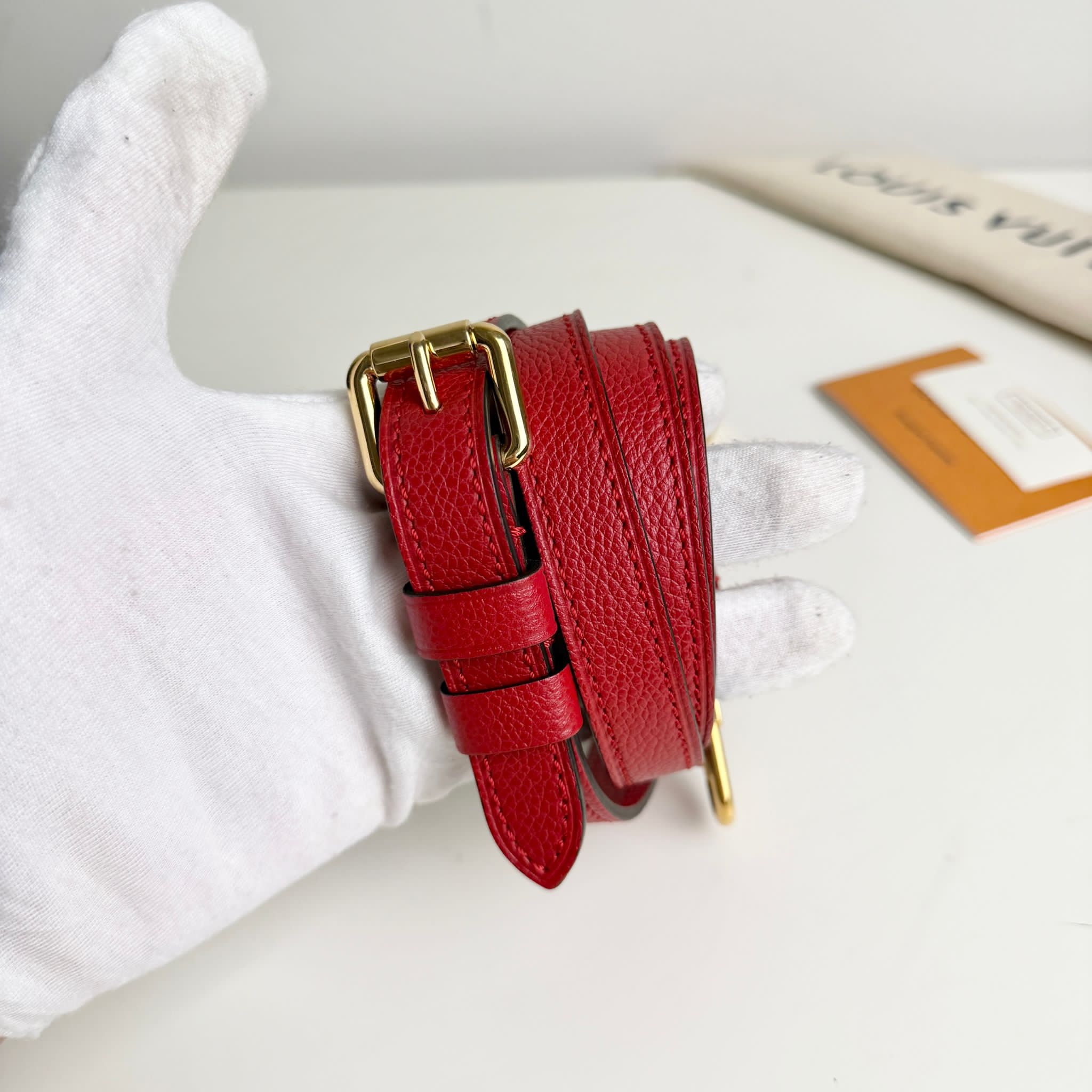 Red leather belt with gold buckle on a white surface