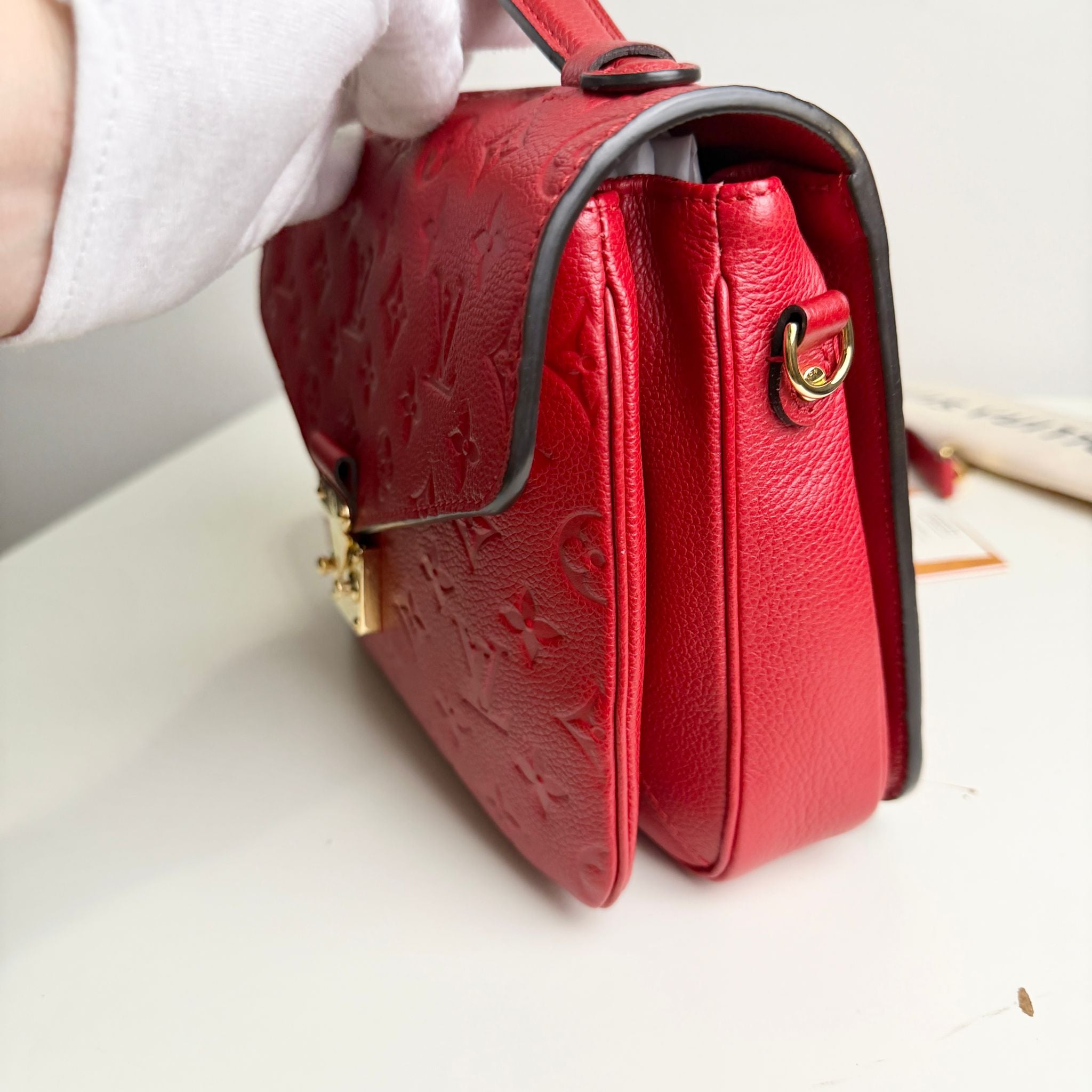 Red handbag with gold accents held by a gloved hand on a light background