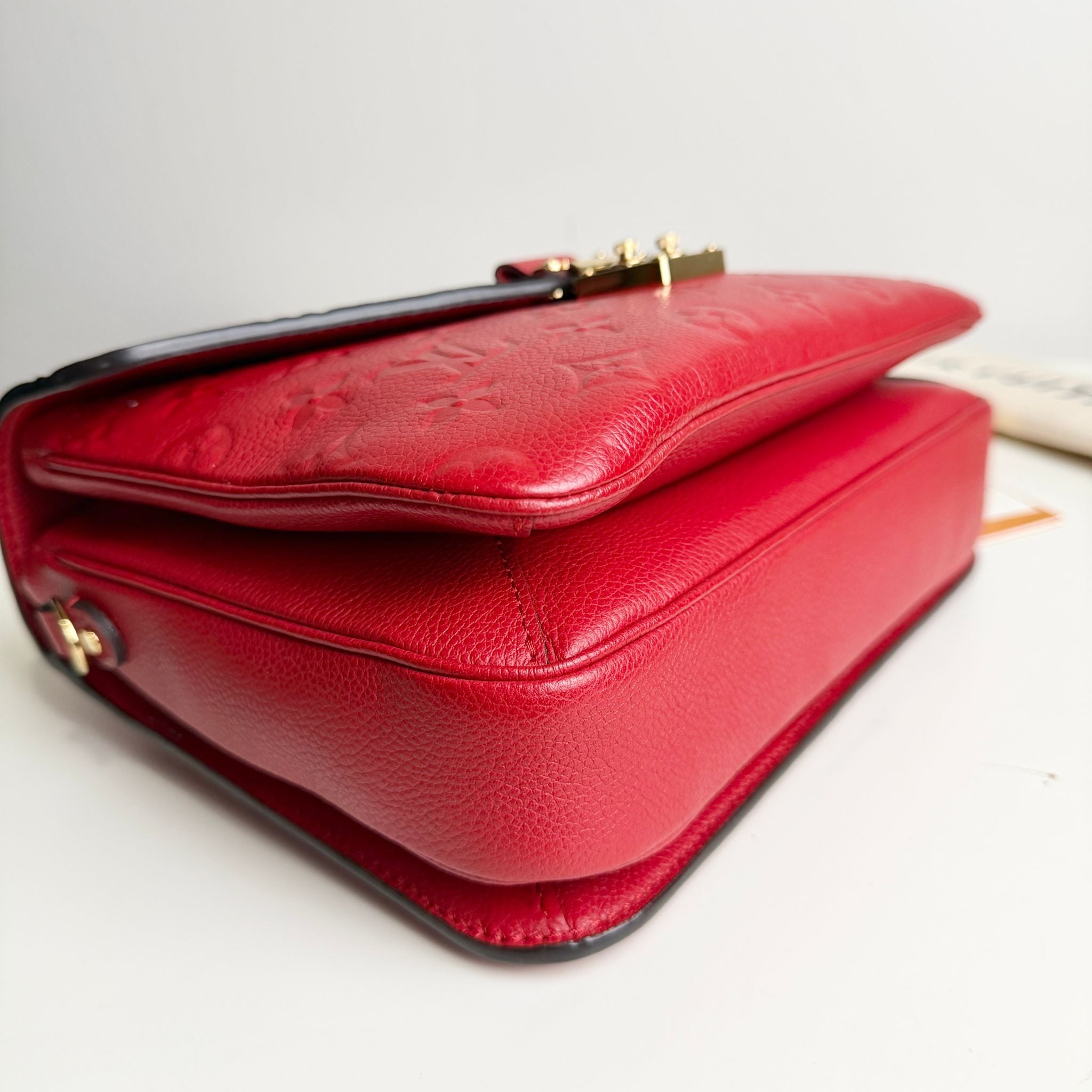 Red leather handbag with gold accents on a light gray background