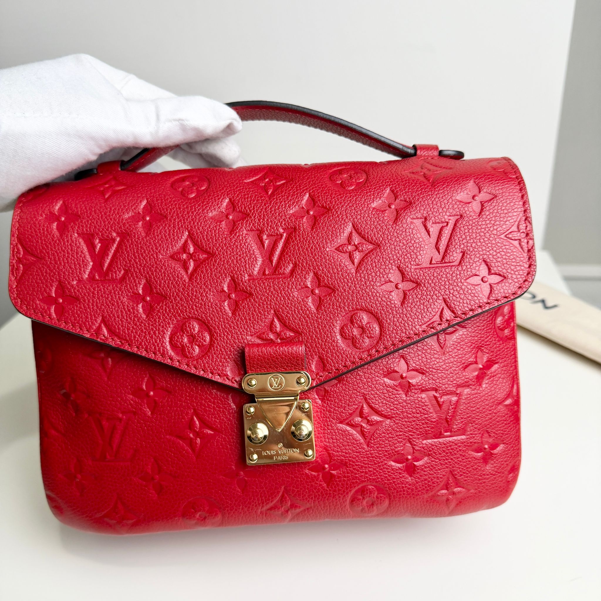 Red handbag with gold lock held by a gloved hand on a white background