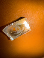 将图片加载到图库查看器，Close-up of a metallic tag with branding on an orange textured surface
