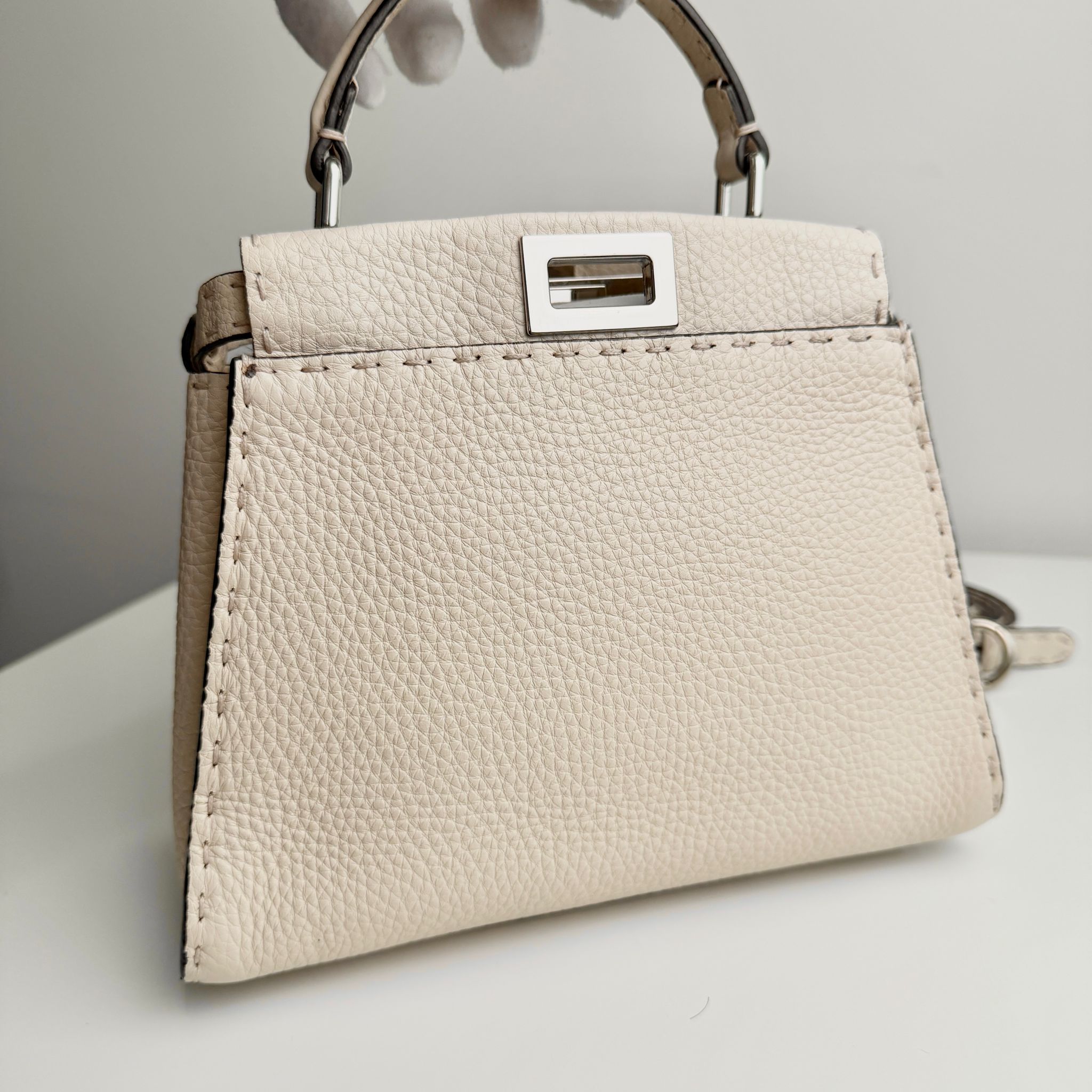 Beige handbag with a silver clasp on a light gray background